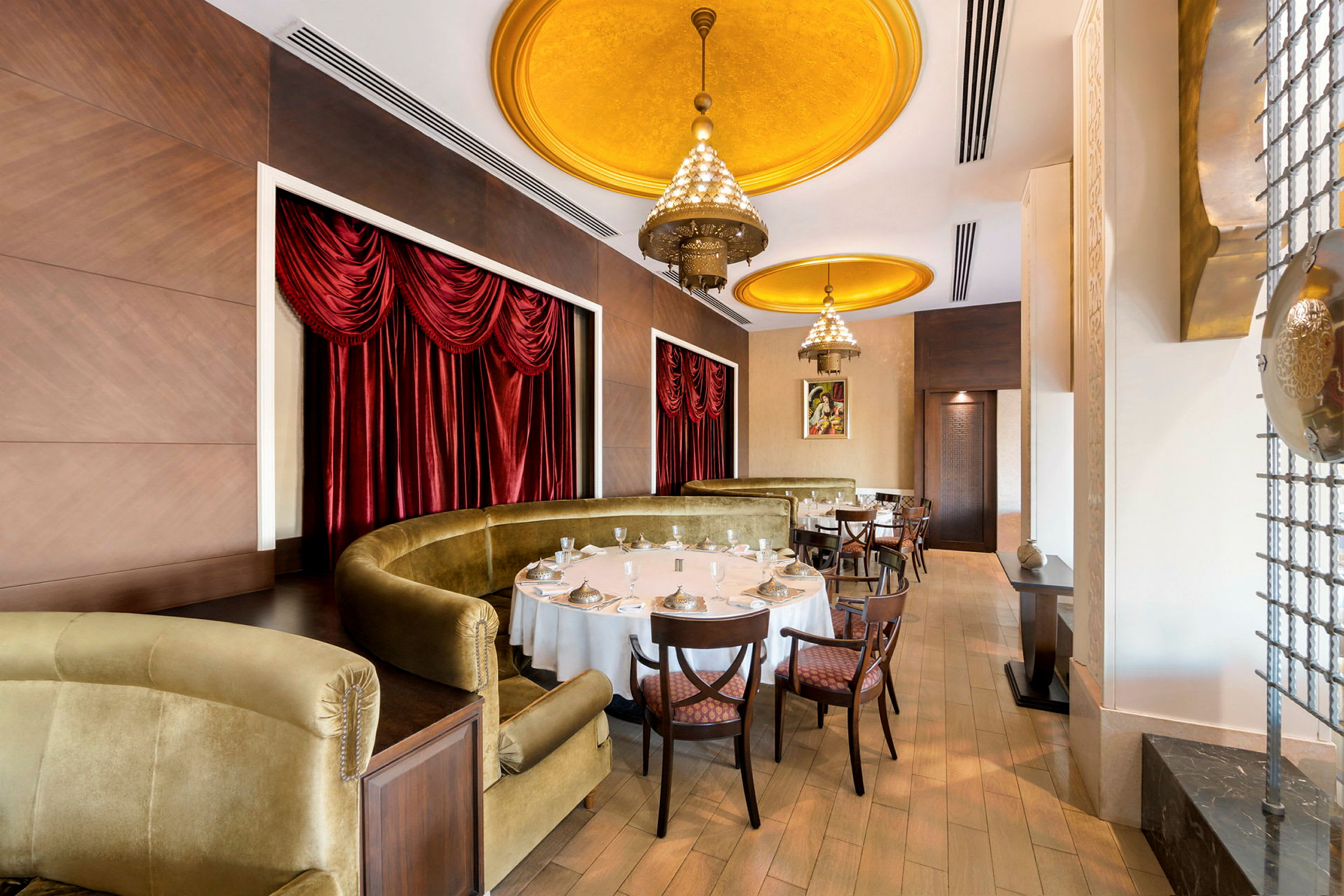 Interiør av en elegant restaurant med gullfargede takdetaljer og røde gardiner. (AI-generert tekst)