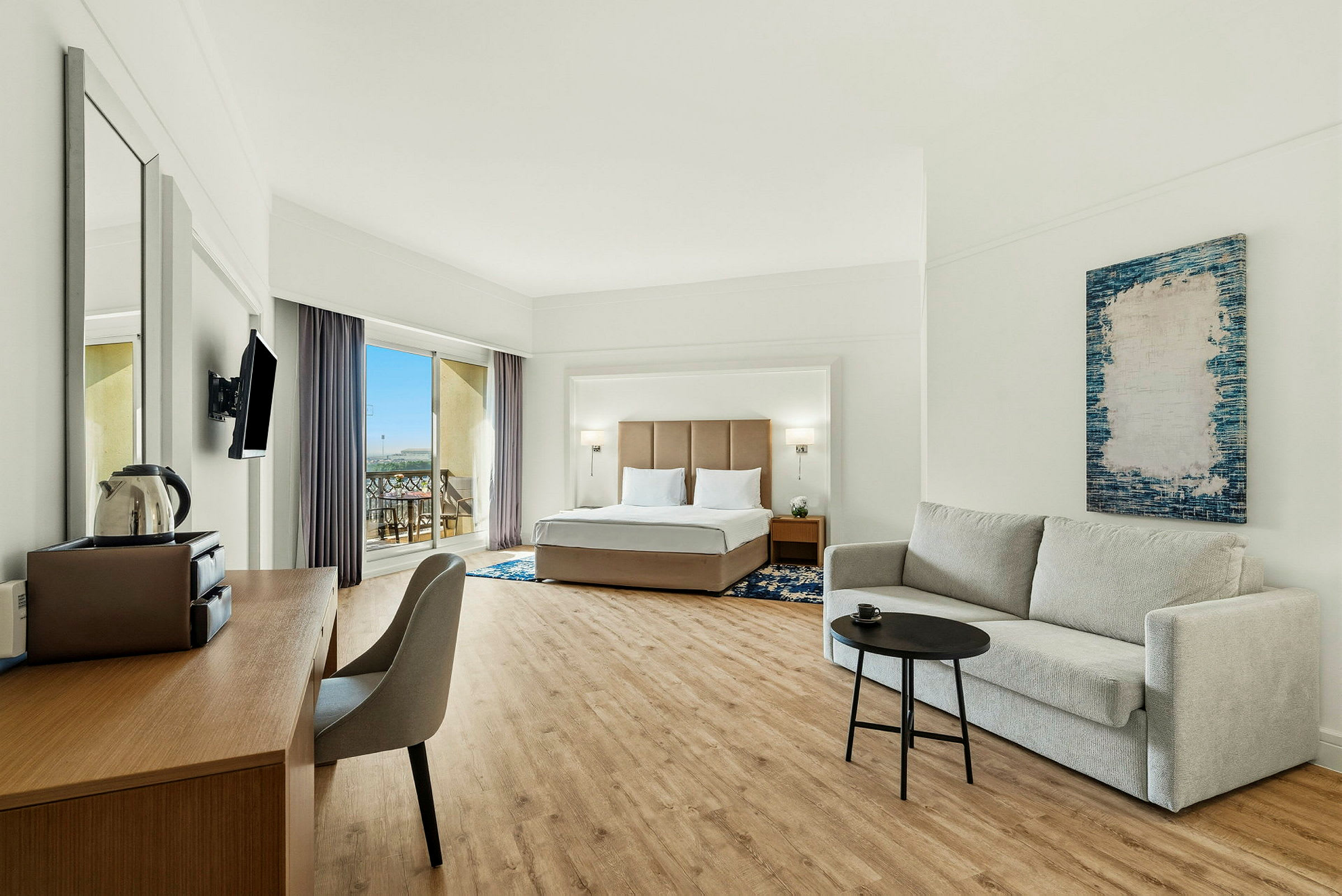Hotellrom med en dobbeltseng, en sofa og et skrivebord, samt en balkong med utsikt. (AI-generert tekst)