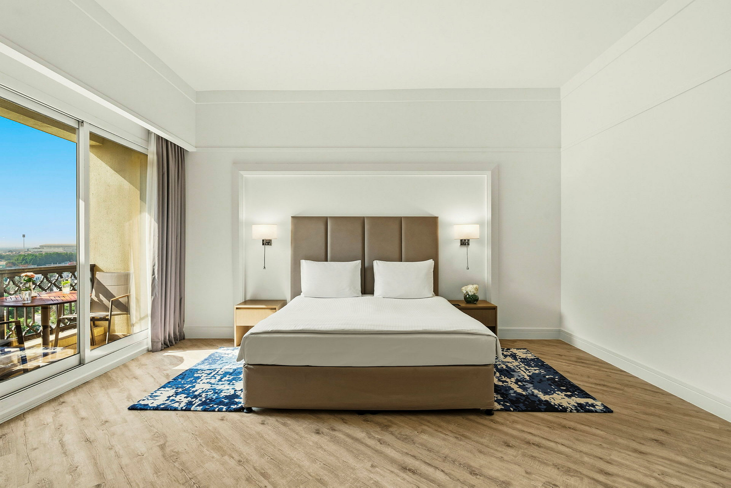 Et hotellrom med en stor seng, to nattbord og en balkong med utsikt. (AI-generert tekst)