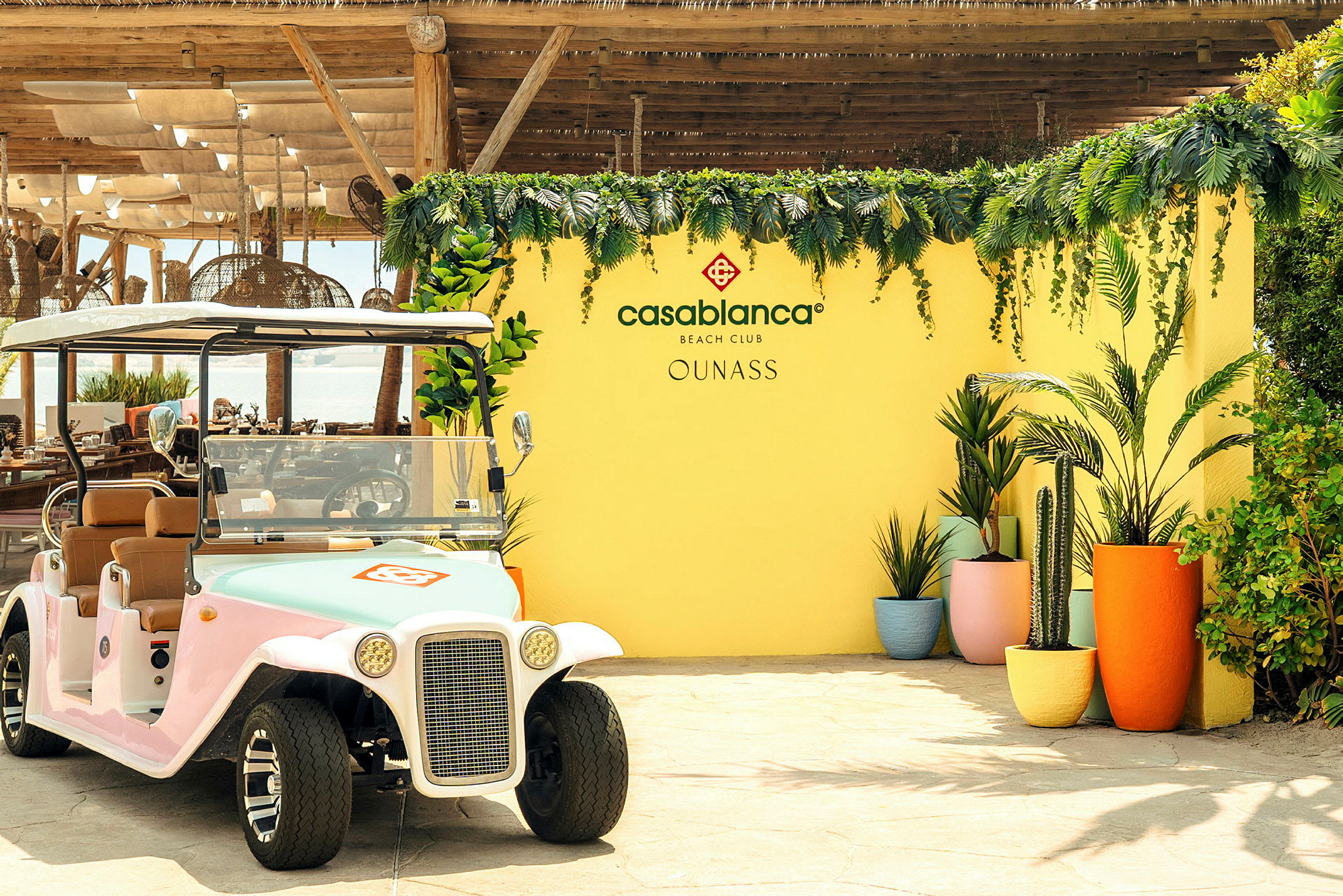 En golfbil står foran en gul vegg dekorert med vegetasjon og blomster, sammen med teksten 'Casablanca Beach Club'. (AI-generert tekst)