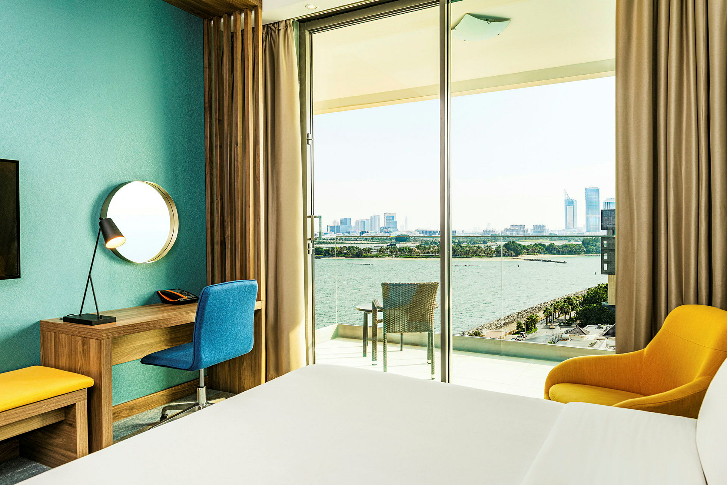 Et hotellrom med utsikt over en elv og byens skyline. Et skrivebord, stol og lenestol er på rommet. (AI-generert tekst)