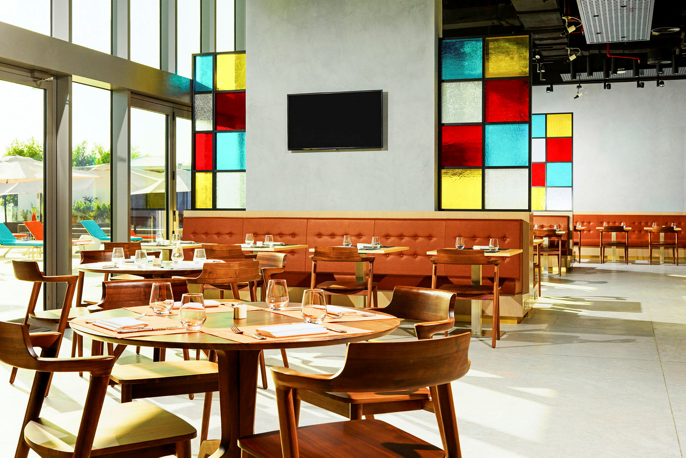 Bilde av en moderne restaurant med fargerike glasspaneler og trebord, dekket til gjester. (AI-generert tekst)