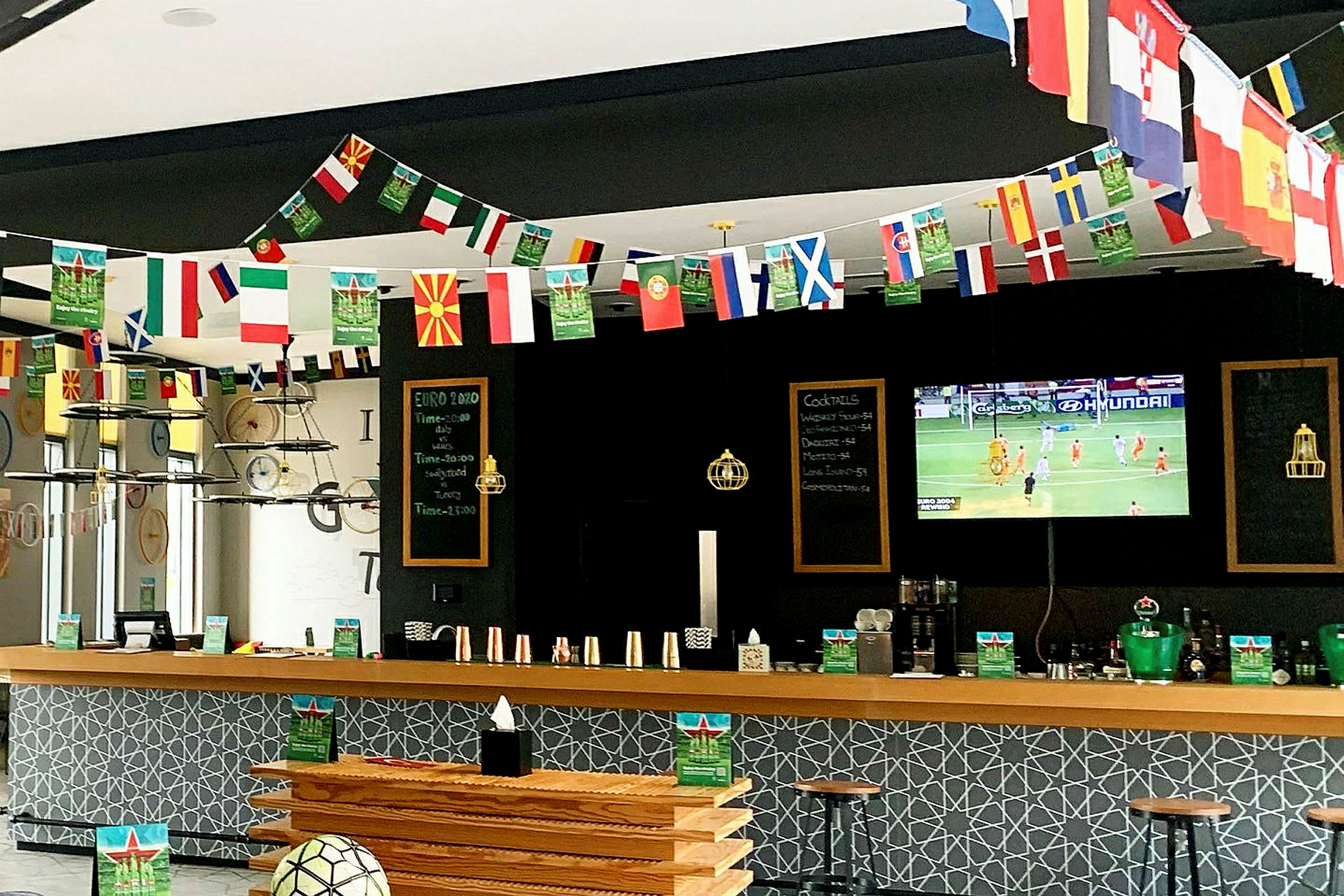 En sportsbar med dekorasjoner av landsflagg og en TV som viser en fotballkamp. (AI-generert tekst)