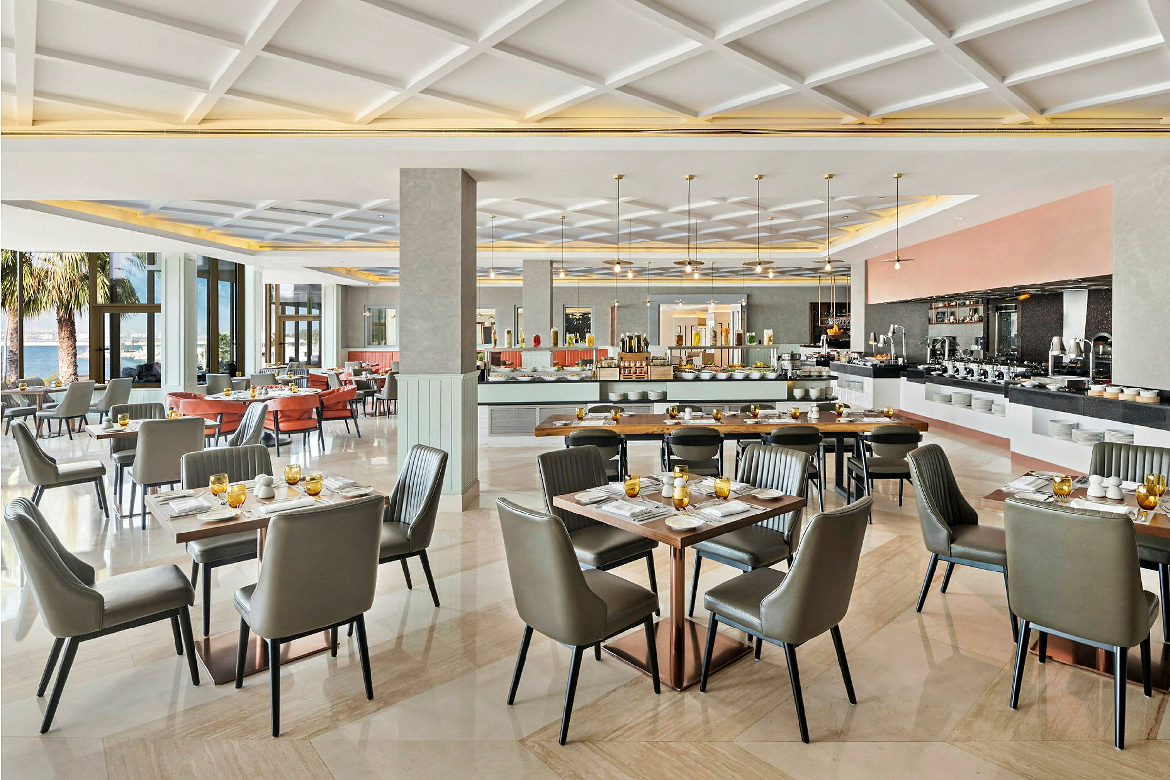 En moderne restaurant med elegant innredede bord og stoler samt store vinduer med utsikt mot trær og utemiljø. (AI-generert tekst)