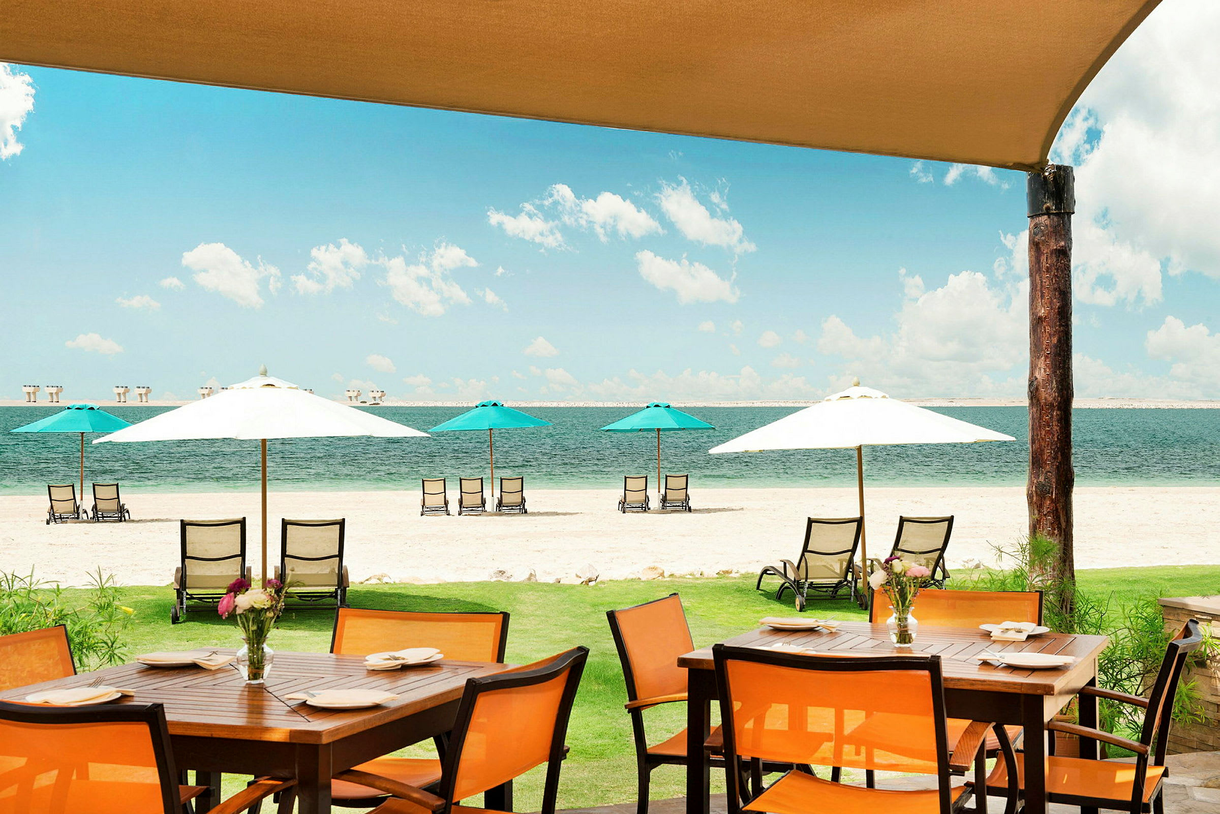 En strandscene med parasoller, solsenger og et spisebord i forgrunnen. (AI-generert tekst)