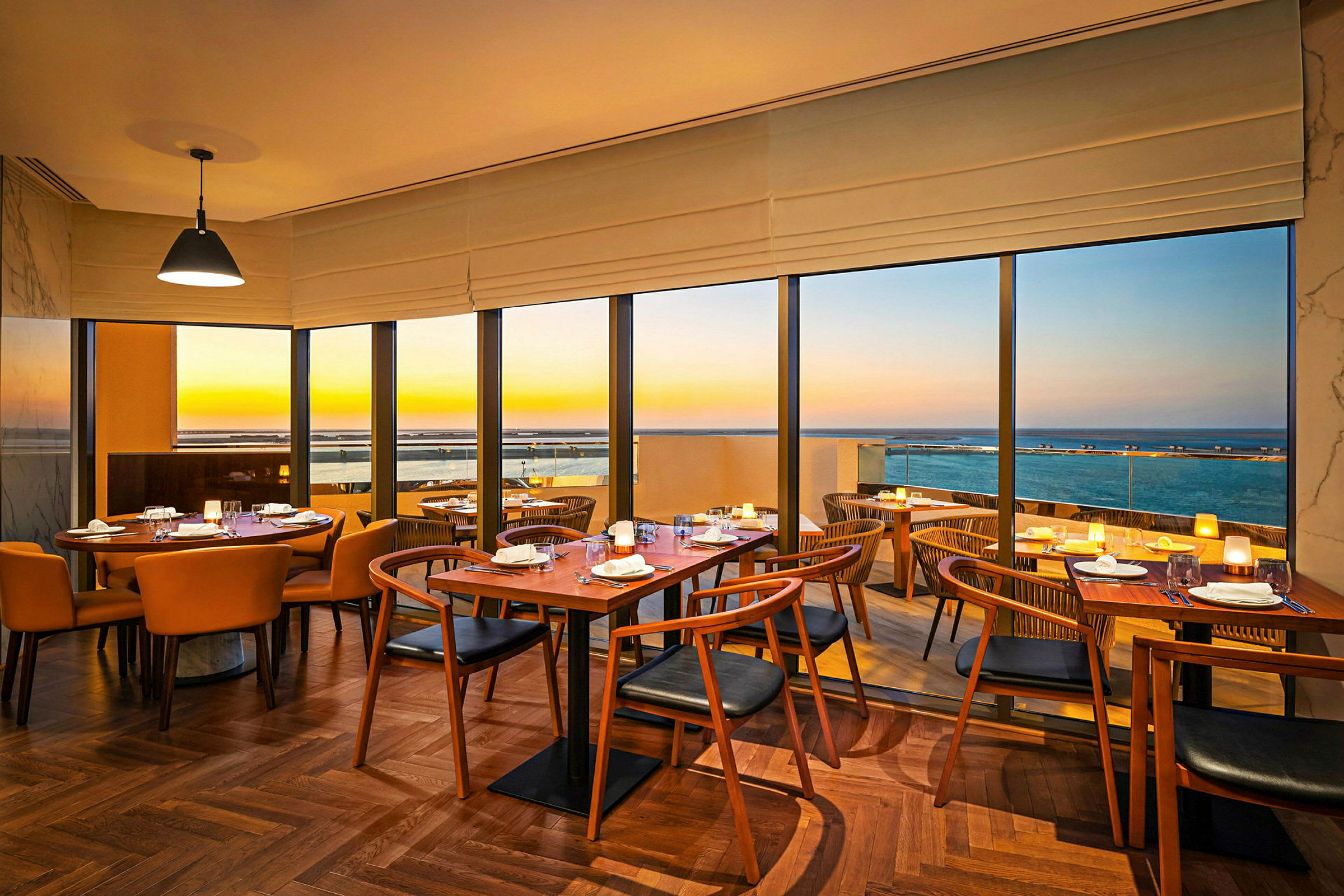 Interiør av en restaurant med store vinduer og havutsikt ved solnedgang. (AI-generert tekst)