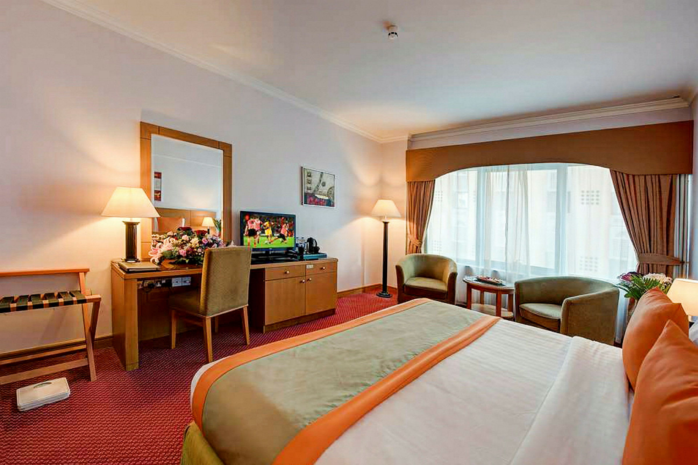 Et hotellrom med en dobbeltseng, to lenestoler foran et stort vindu og en TV på en kommode ved siden av et skrivebord med en stol. (AI-generert tekst)