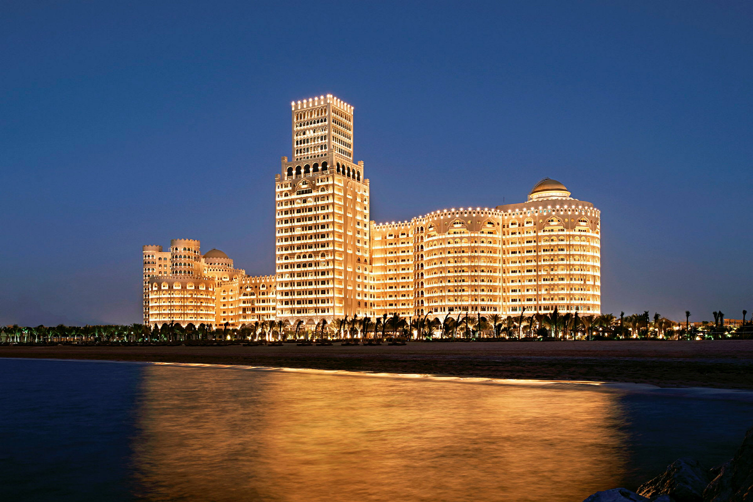 Bildet viser en stor bygning med mange vinduer som er opplyst mot en mørk nattehimmel. (AI-generert tekst)