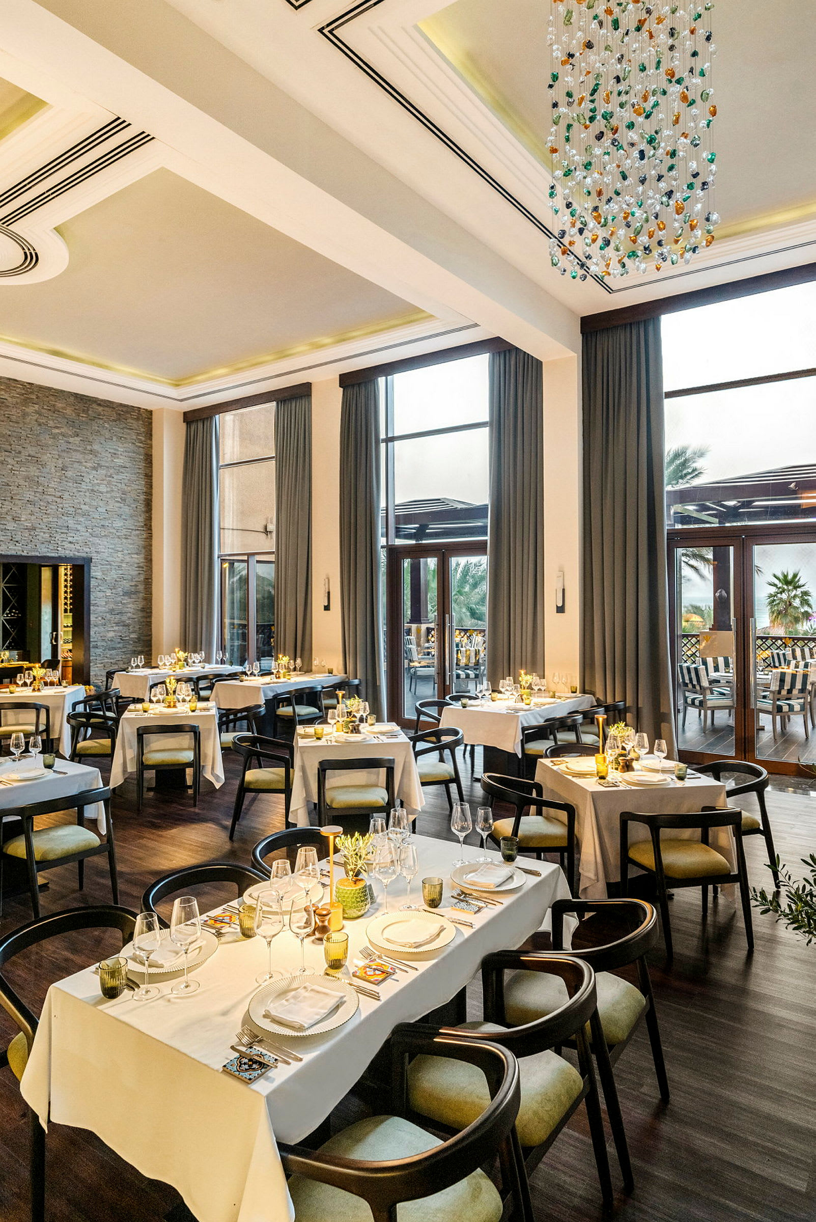 En elegant restaurant med dekkede bord for middag, store vinduer og en lysekrone i taket. (AI-generert tekst)