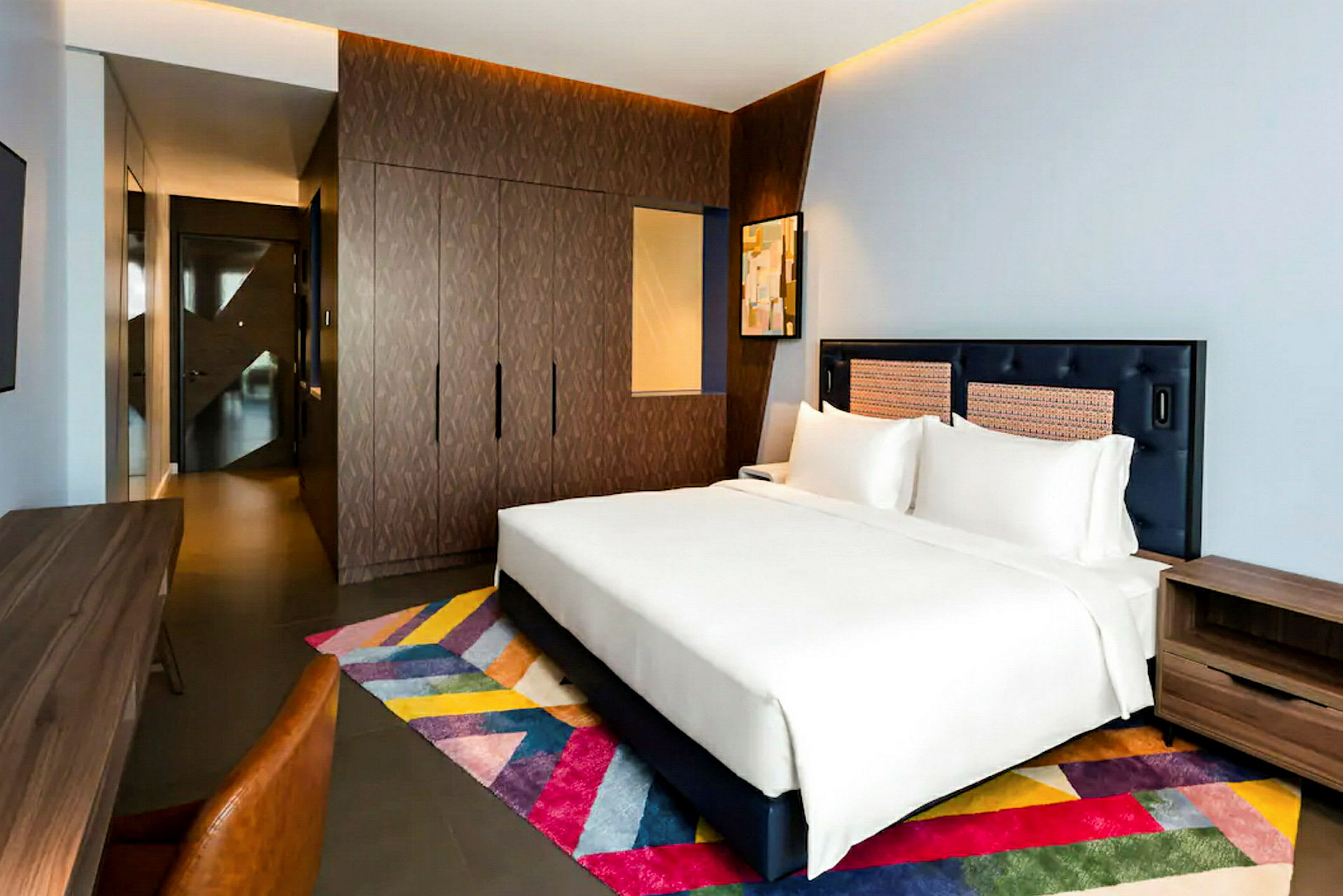 Et moderne innredet hotellrom med en stor dobbeltseng og et fargerikt teppe. (AI-generert tekst)
