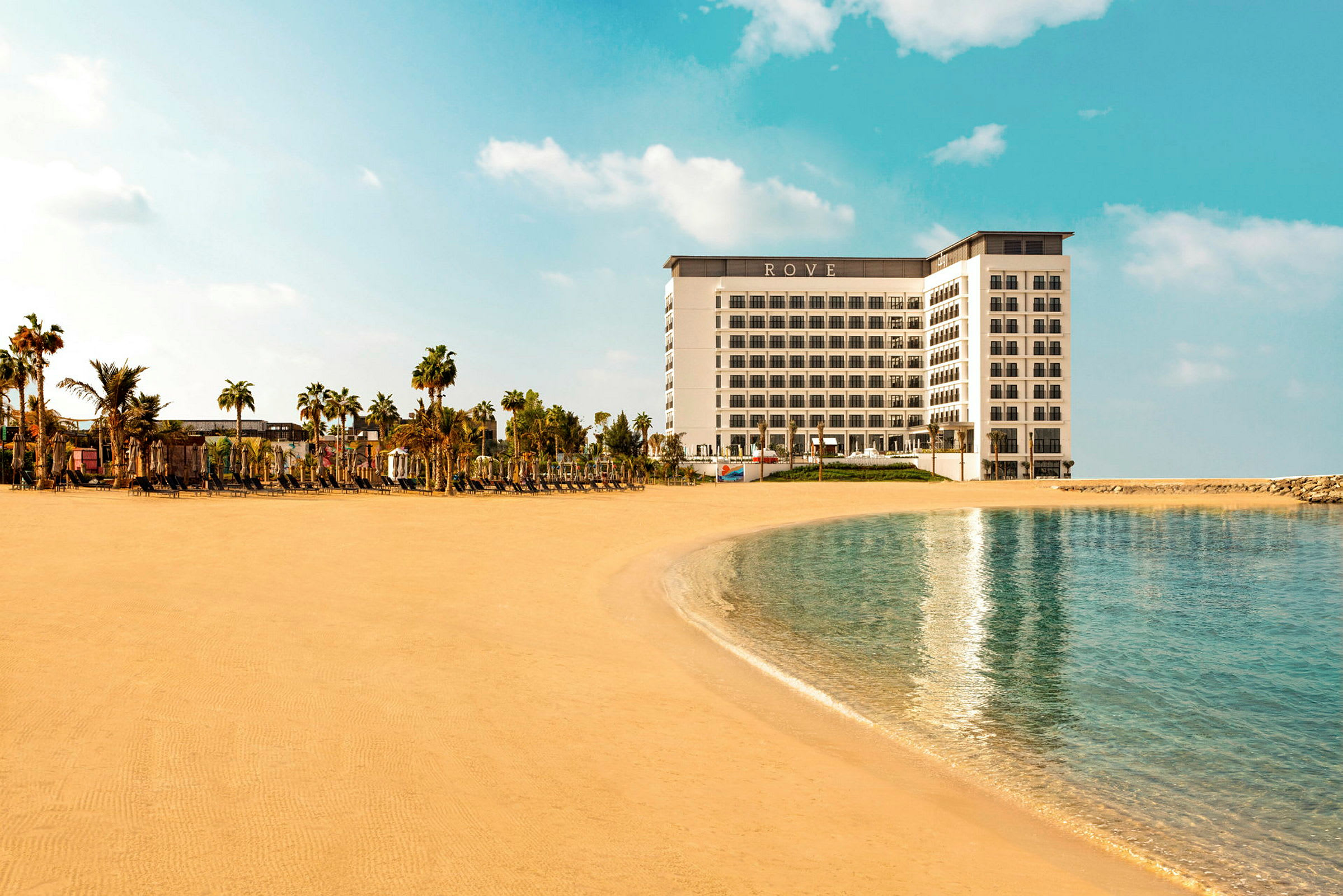 Hotellet Rove plassert ved en sandstrand, omgitt av palmer. (AI-generert tekst)