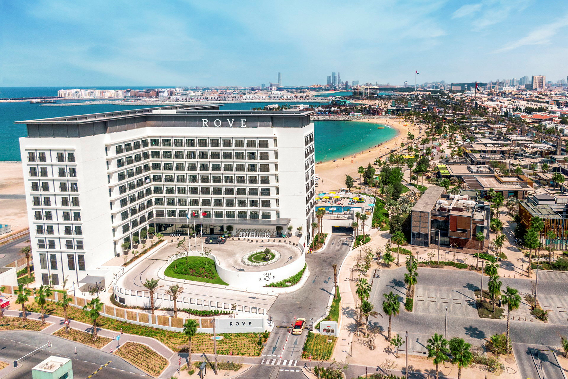 Et hotell med en hvit fasade ved en strand med blått vann. (AI-generert tekst)