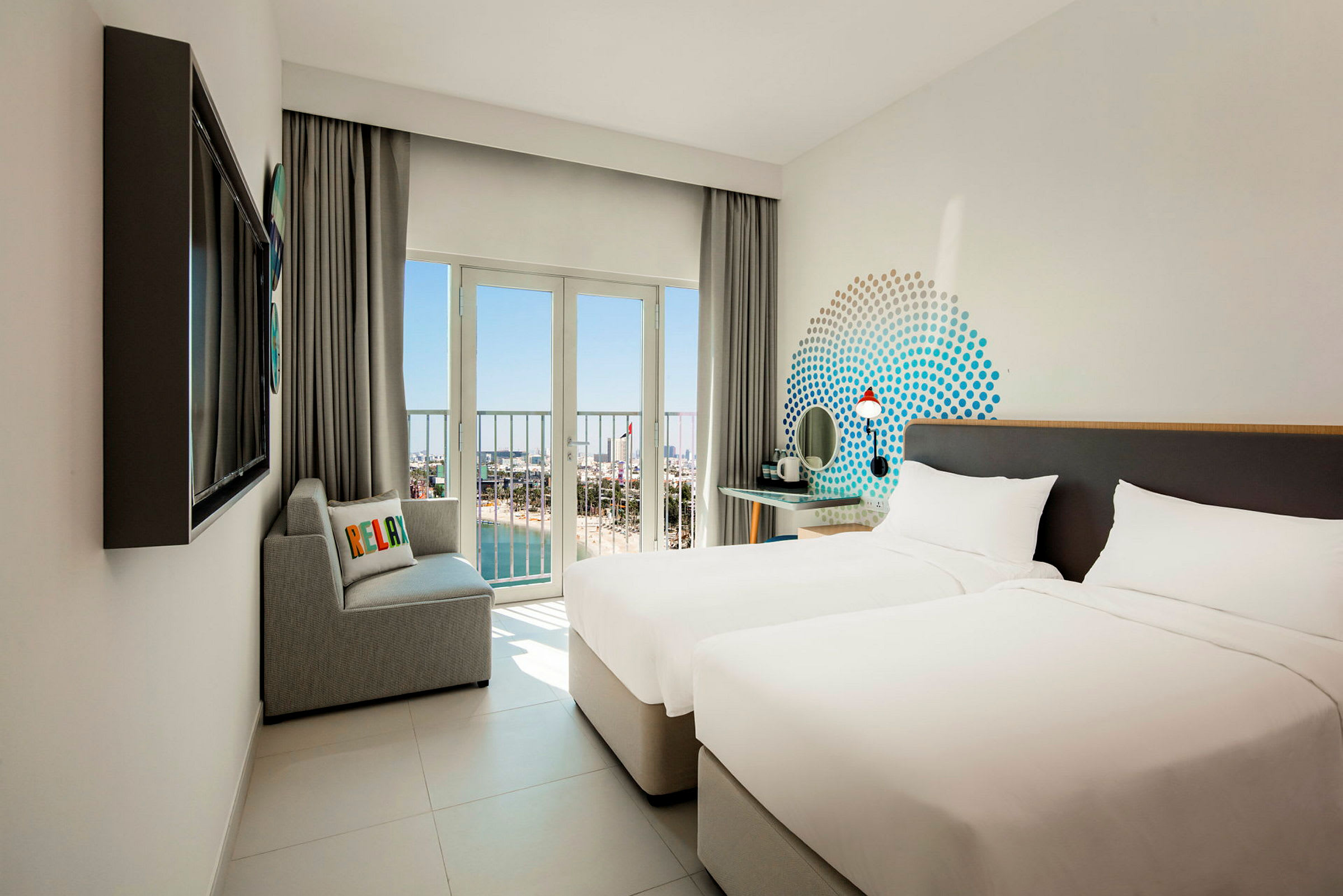 Hotellrom med to enkeltsenger, en sofa og utsikt gjennom store vinduer mot stranden og havet. (AI-generert tekst)