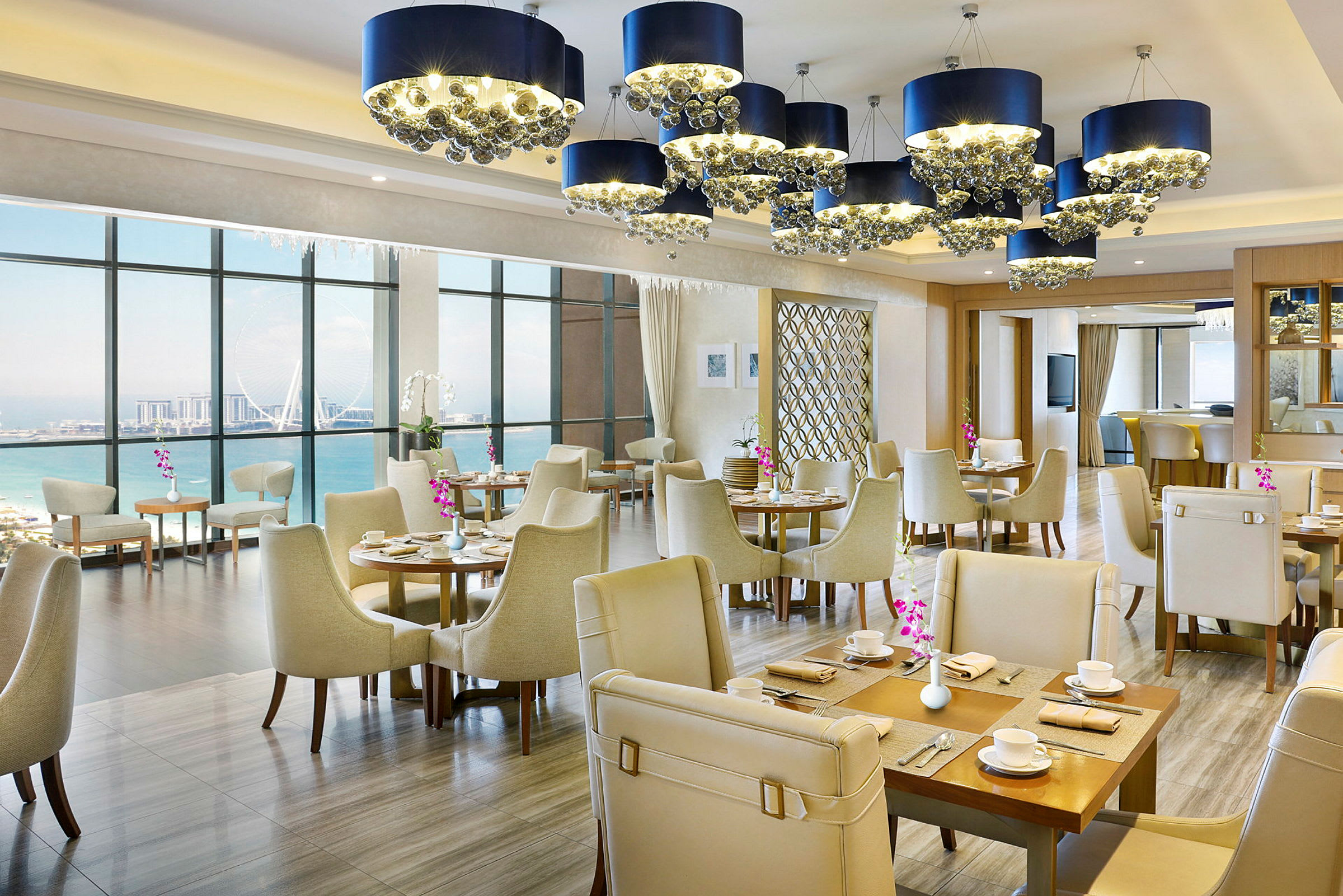 Interiør av en elegant restaurant med havutsikt, lyse møbler og dekorative lysekroner. (AI-generert tekst)