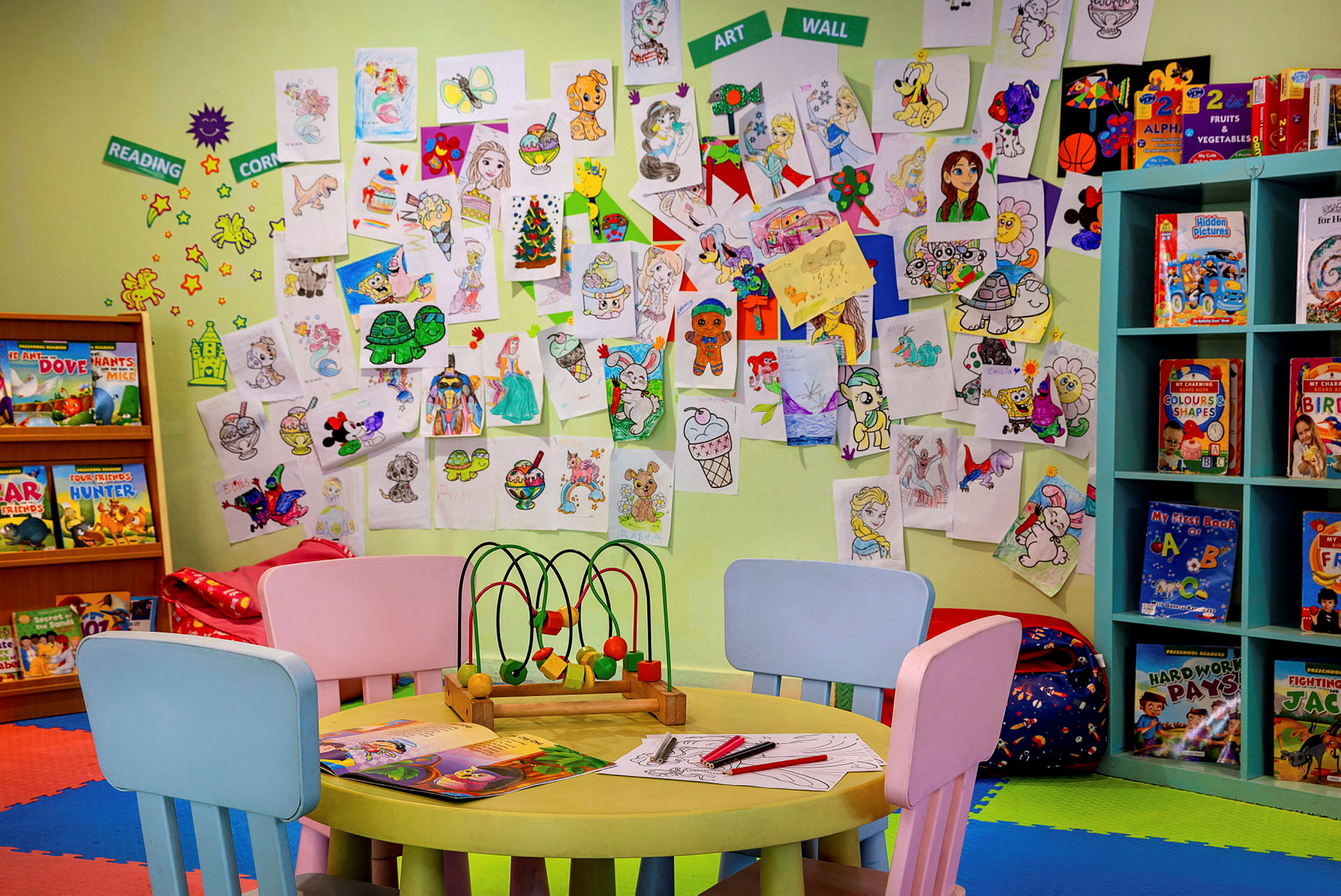 Et barnerom med en vegg dekket av tegninger og hyller med bøker. (AI-generert tekst)