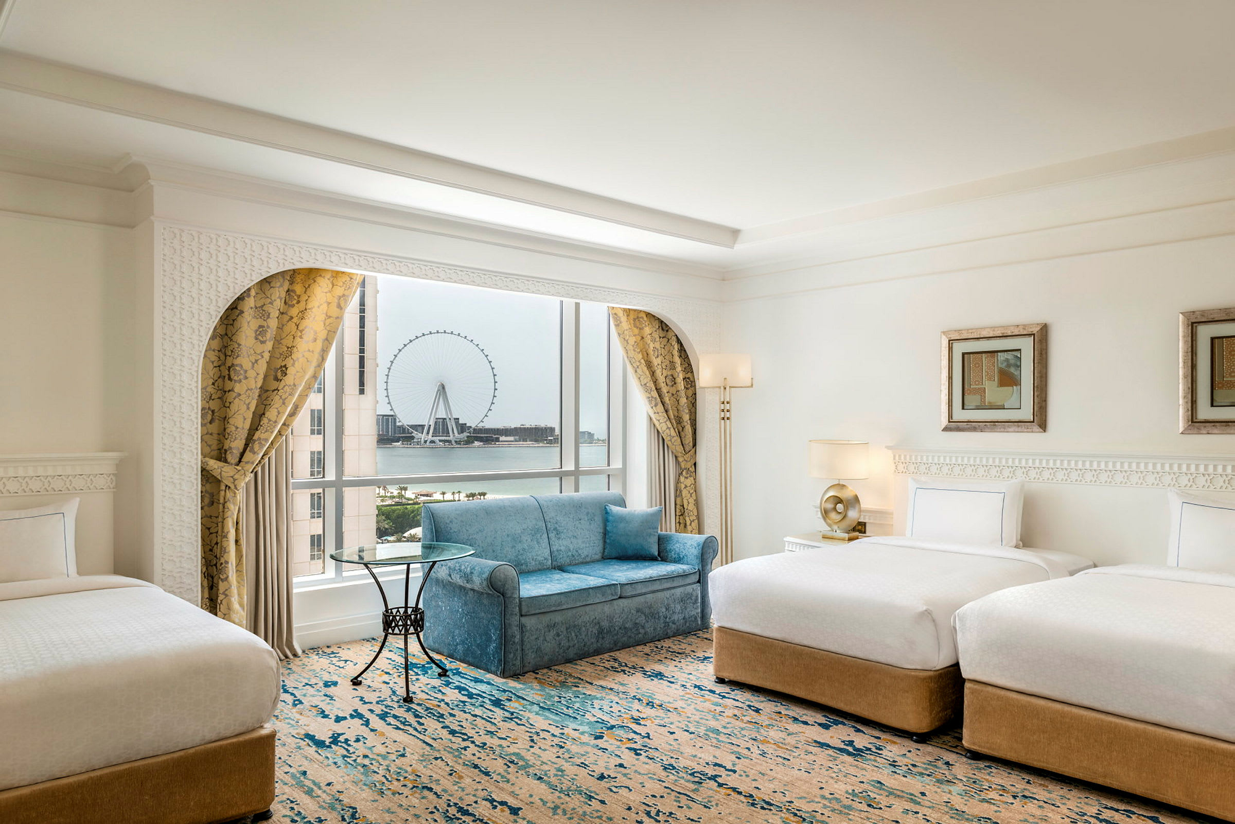 Et elegant hotellrom med to enkeltsenger, en sofa, et vindu med utsikt over et stort pariserhjul og gardiner. (AI-generert tekst)