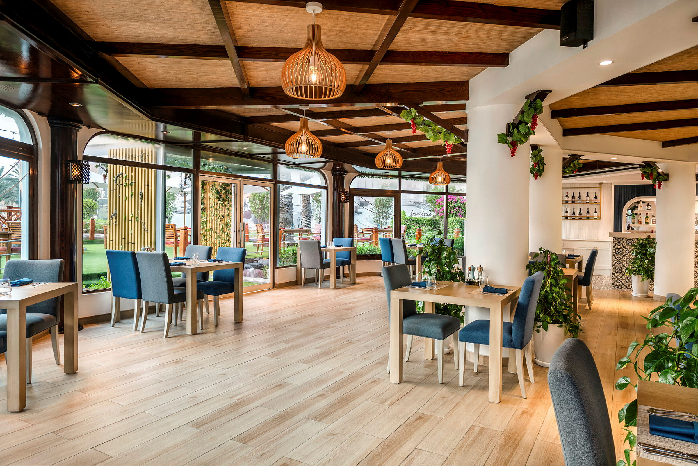 En lys restaurant med bord og stoler i moderne tredesign, grønne planter og store vinduer med utsikt mot en hage. (AI-generert tekst)