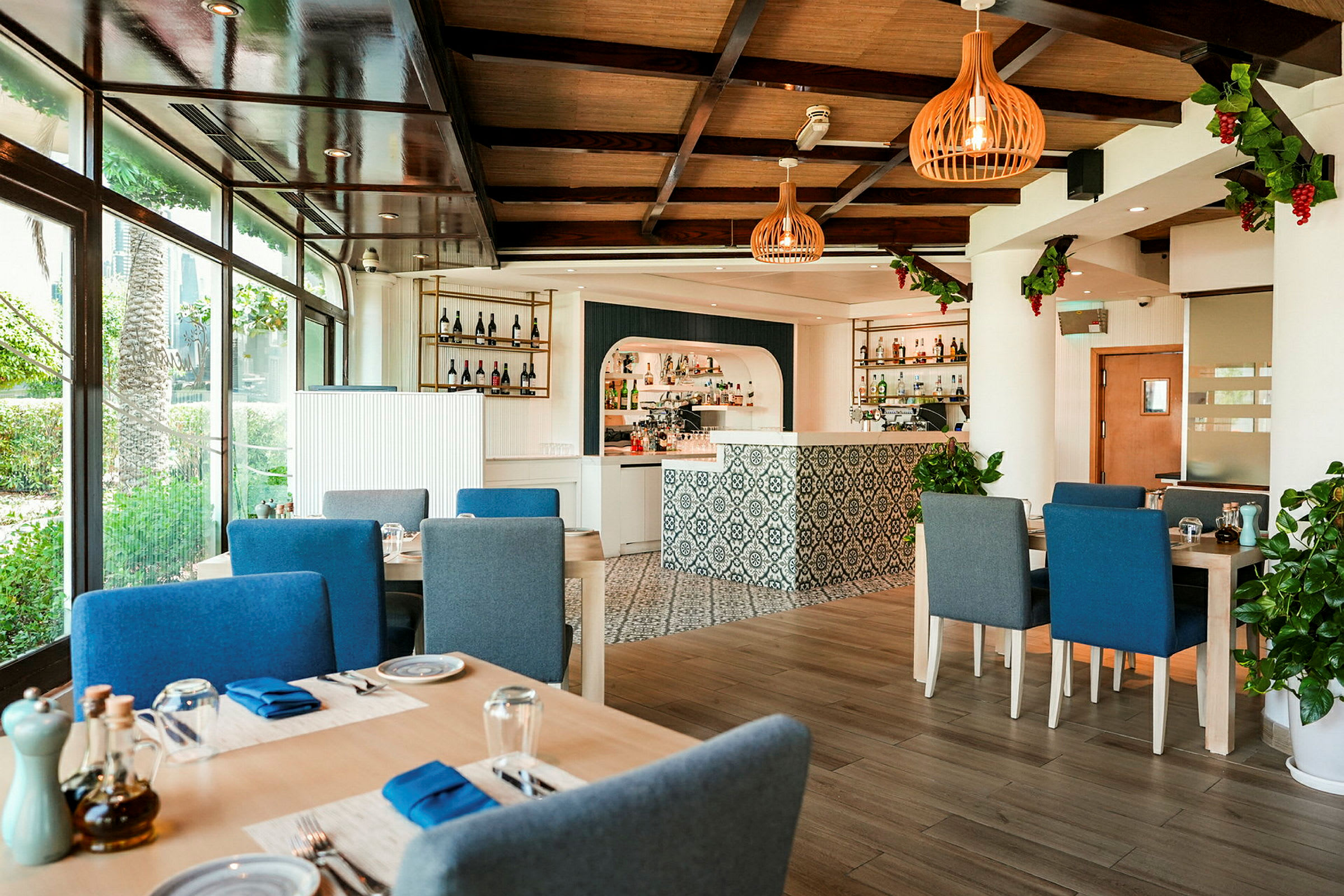 Et lyst og moderne innredet restaurantområde med blå stoler rundt bord, store vinduer og en dekorativ bardisk. (AI-generert tekst)