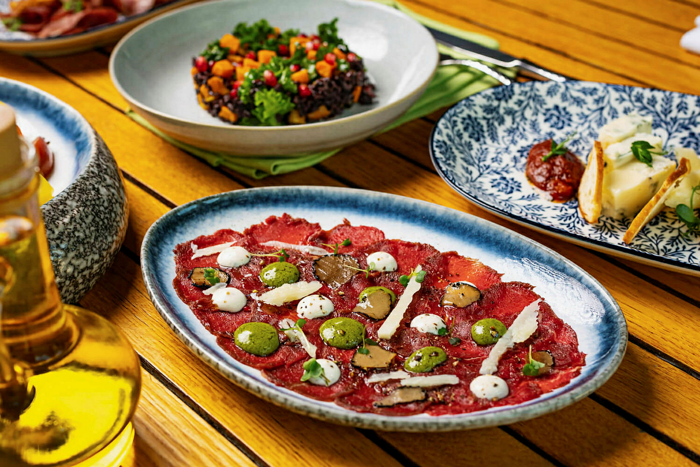 Et bord med forskjellige retter, inkludert en tallerken med carpaccio, en bolle salat og tallerkener med ost og tilbehør. (AI-generert tekst)