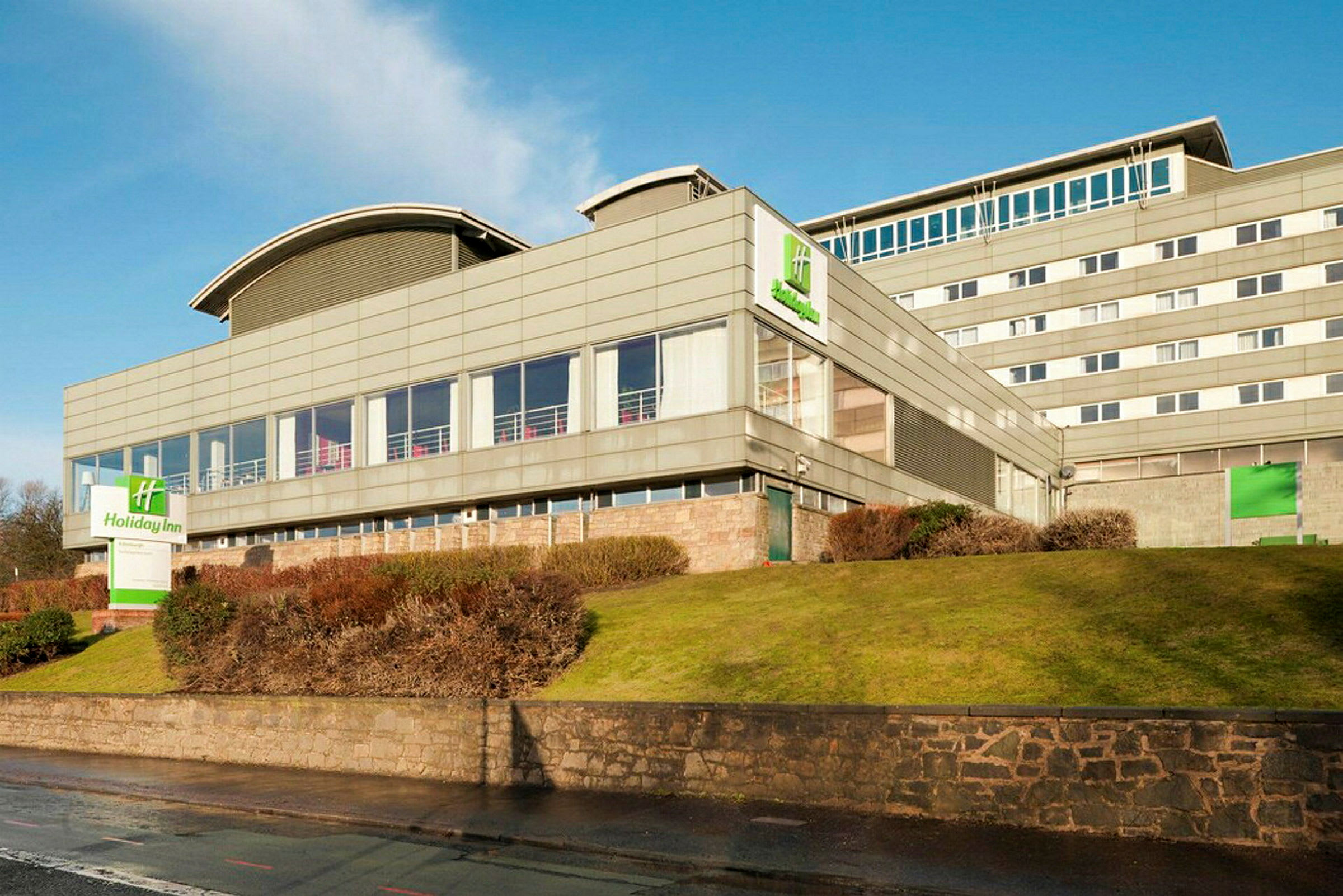 Holiday Inn-hotell i en moderne bygning med omkringliggende plen og busker. (AI-generert tekst)