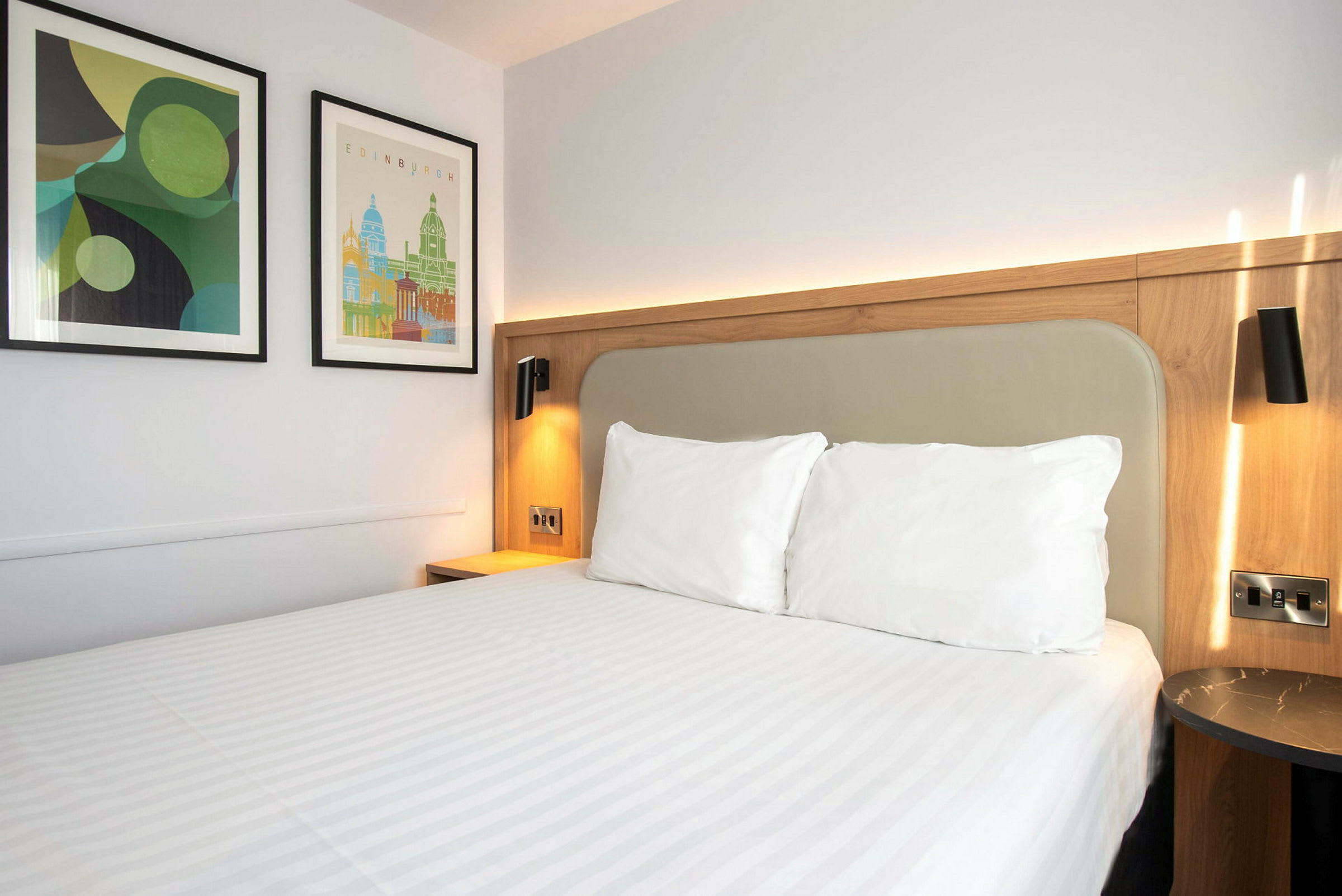 En hotellromseng med hvitt sengetøy og to bilder på veggen. (AI-generert tekst)