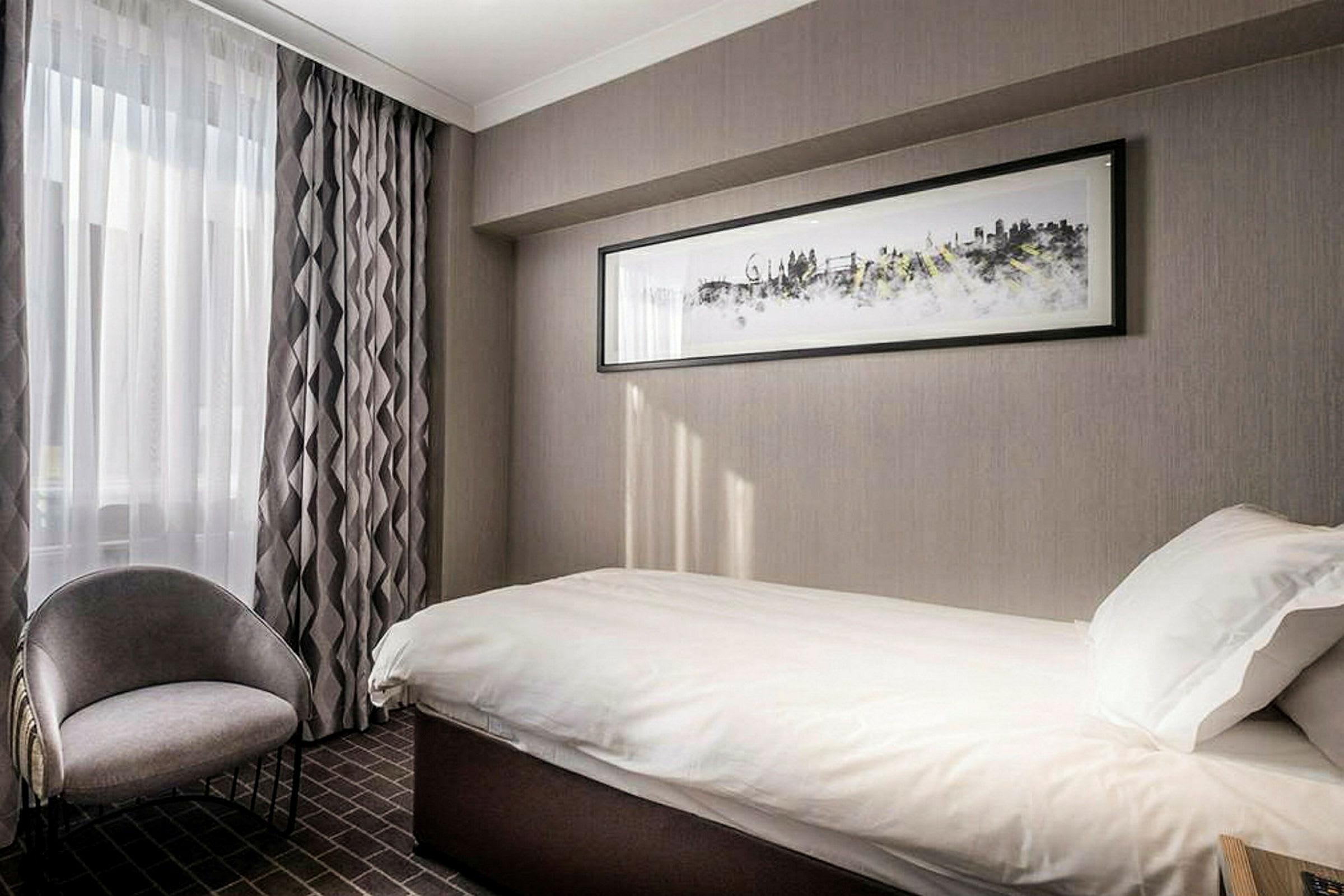 Hotellrom med enkeltseng og stol, dekorert i gråtoner. (AI-generert tekst)