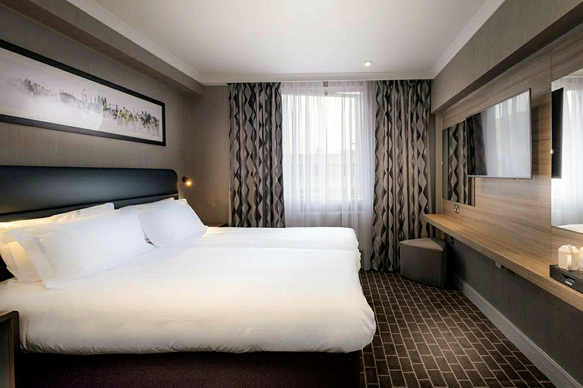 Moderne hotellrom med en dobbeltseng, veggmontert TV og vindu med gardiner. (AI-generert tekst)