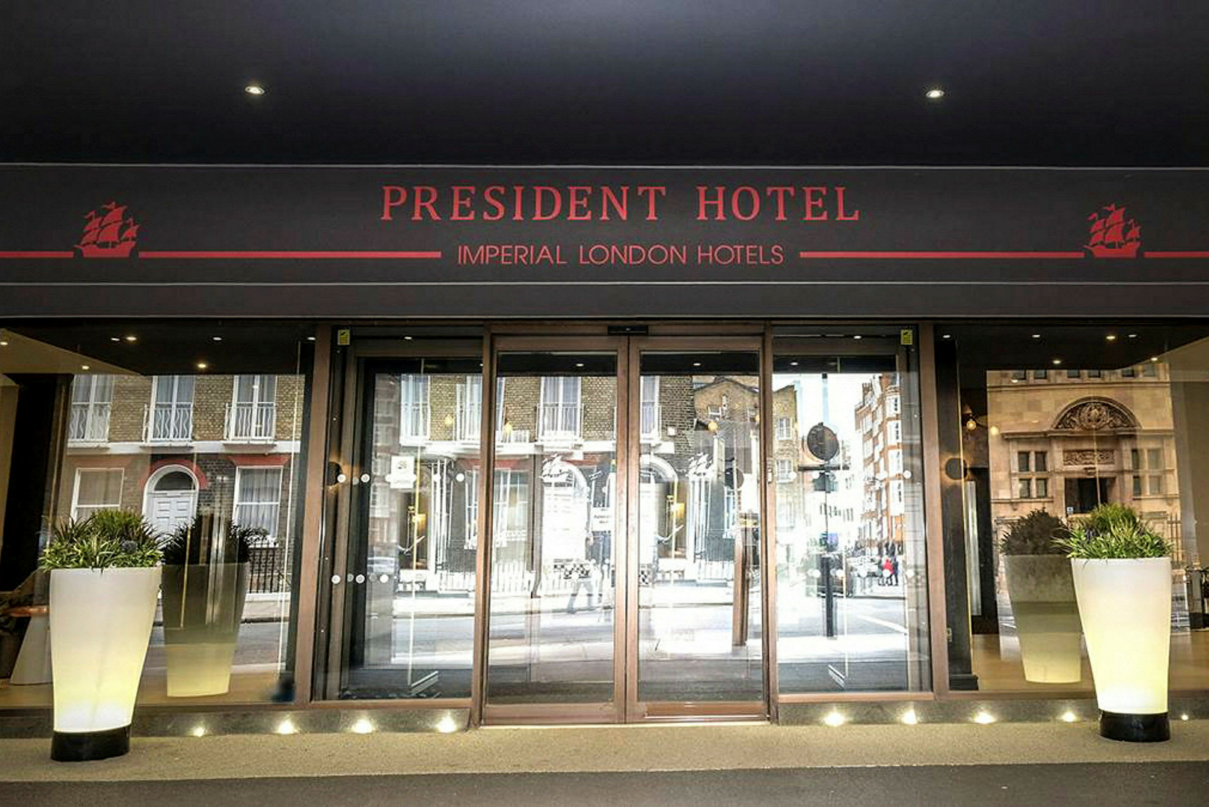 Hovedinngangen til President Hotel med glassdører og blomsterpotter. (AI-generert tekst)