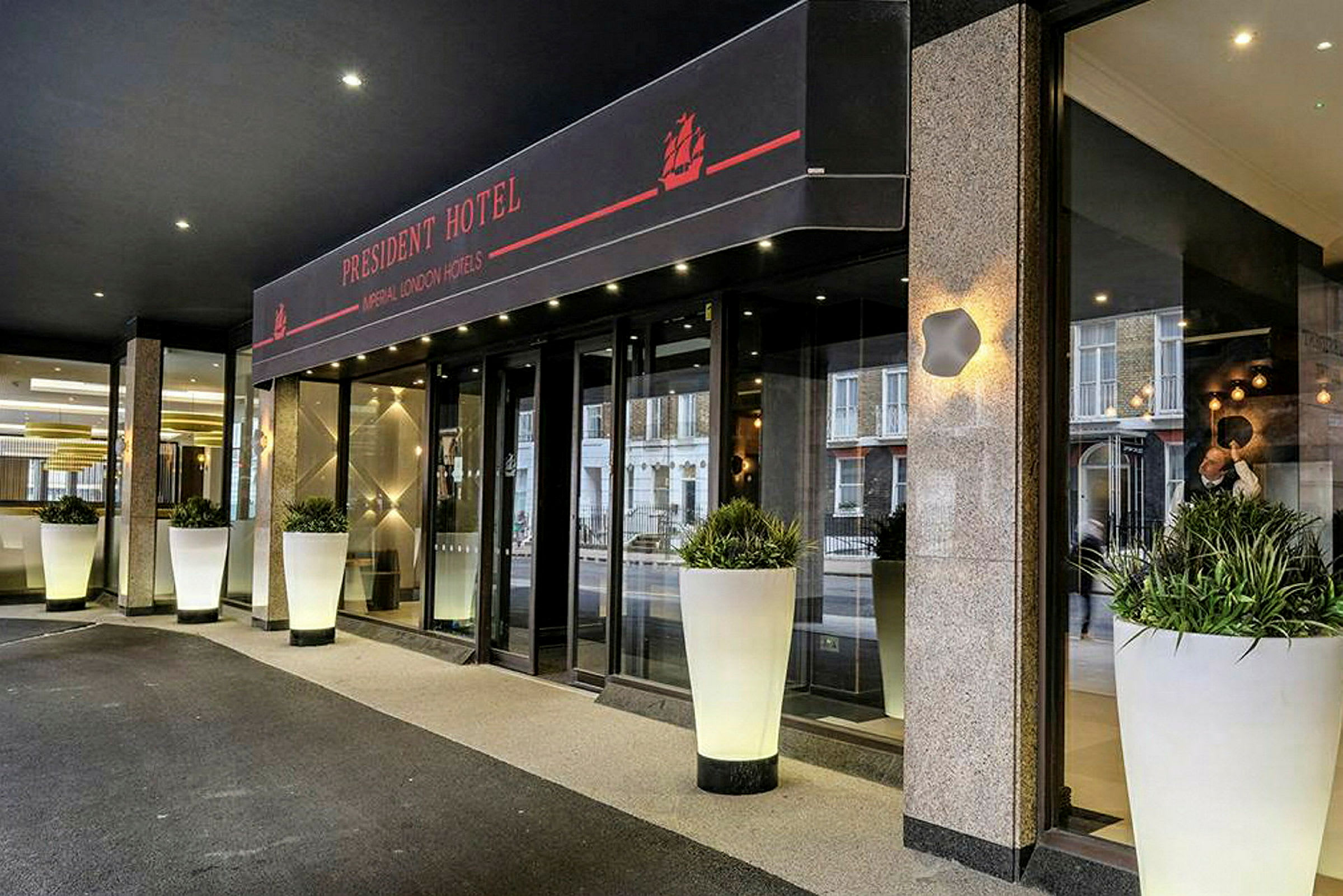 Inngangen til President Hotel, med store hvite blomsterpotter. (AI-generert tekst)