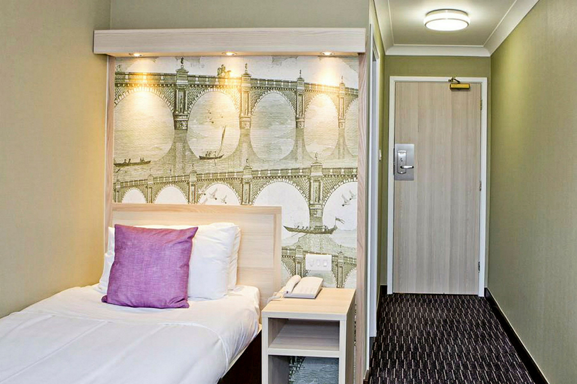 Et hotellrom med en enkeltseng og en veggdekorasjon med bro-motiv. (AI-generert tekst)
