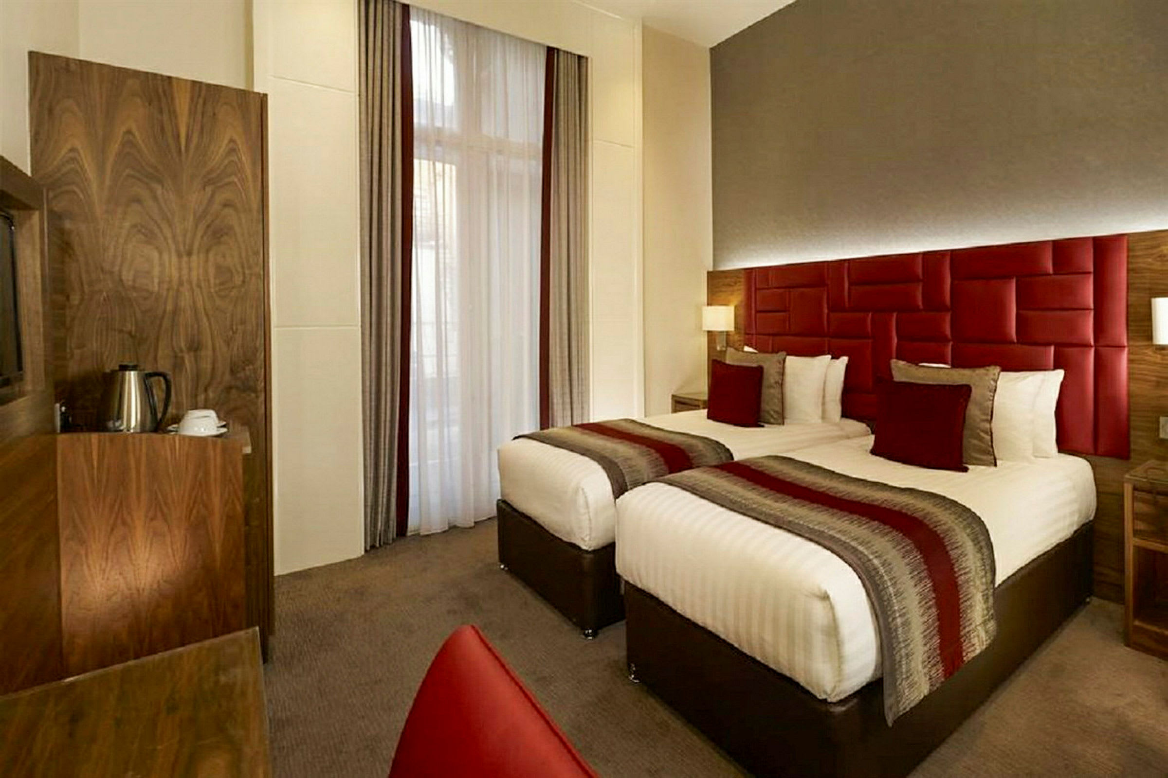 Hotellrom med to enkeltsenger, røde dekorasjoner og en kaffetrakter i hjørnet. (AI-generert tekst)