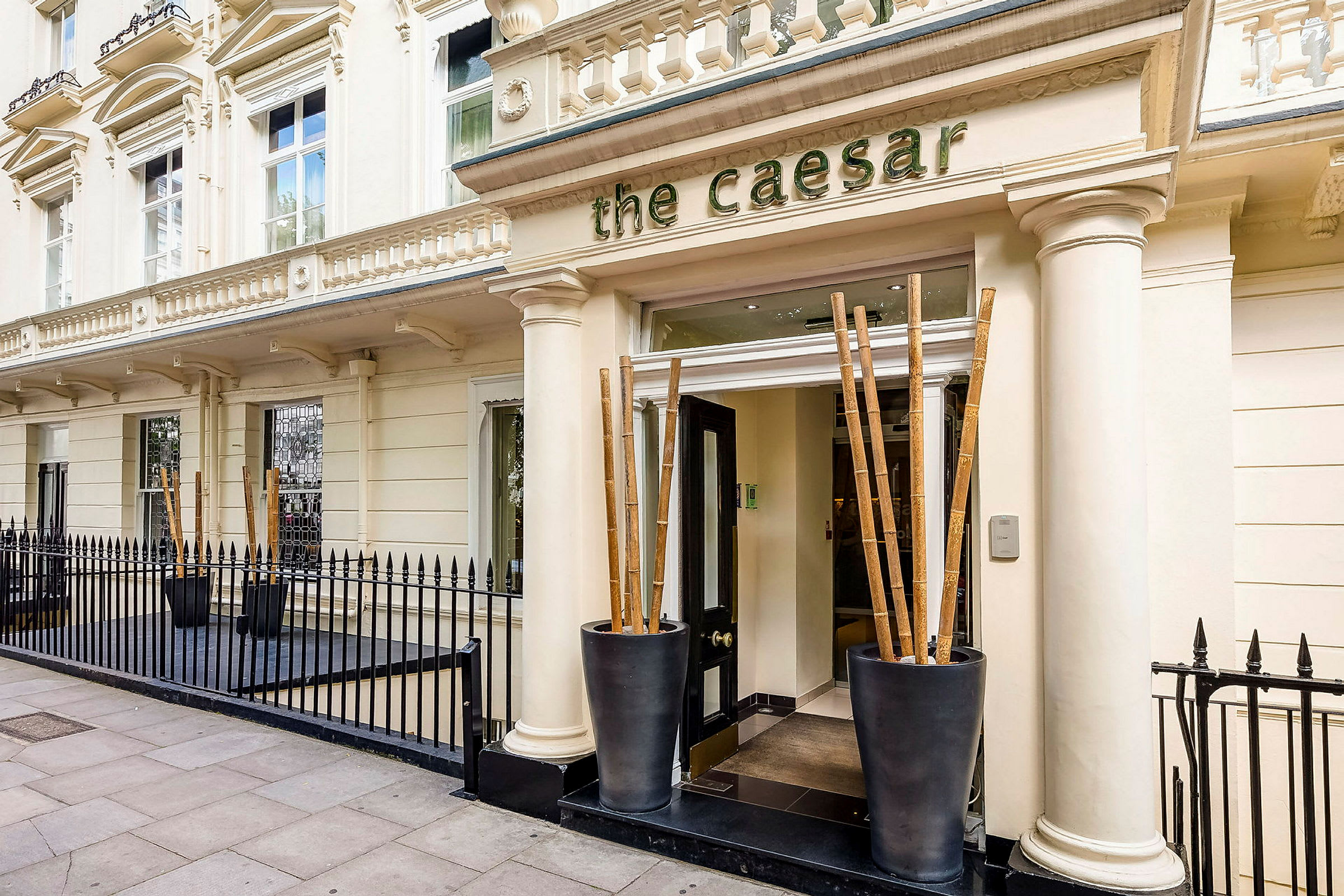 Fasade med inngang til hotell The Caesar, omgitt av svart smijernsrekkverk. (AI-generert tekst)
