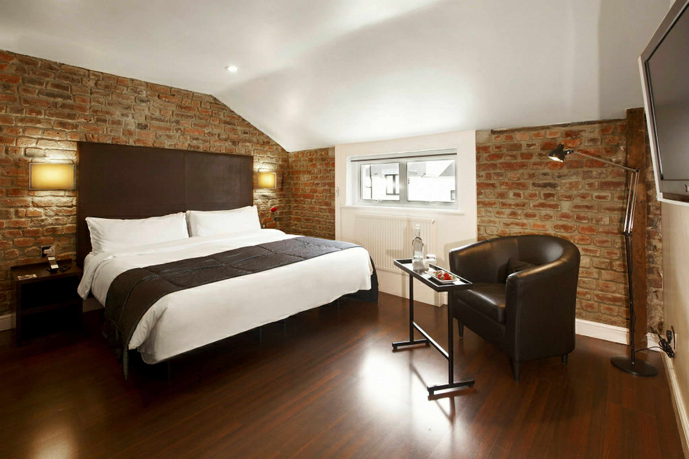 Hotellrom med en stor seng, murvegger og moderne innredning. (AI-generert tekst)