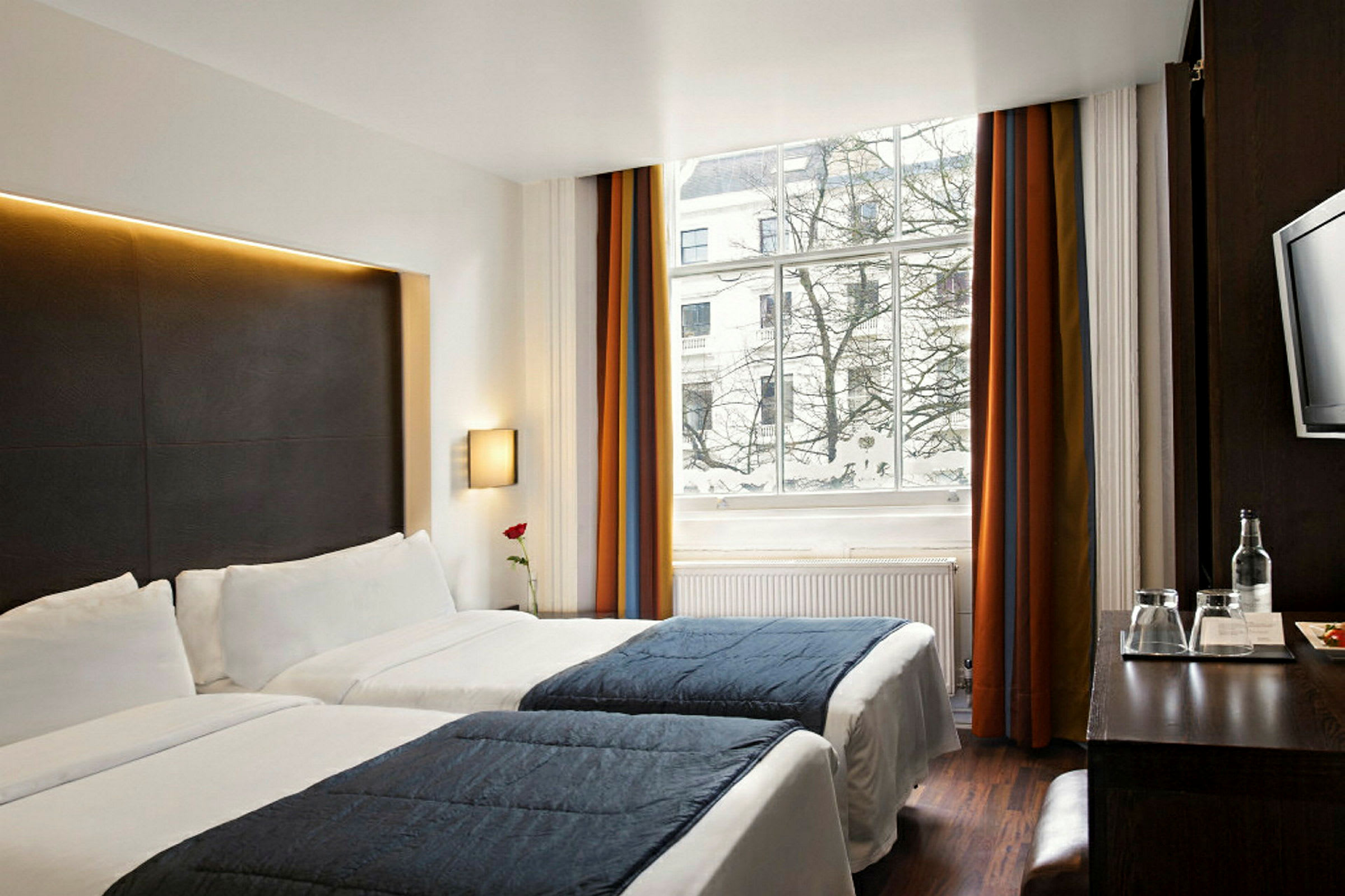 Hotellrom med to enkeltsenger, store vinduer og utsikt over snødekte trær. (AI-generert tekst)