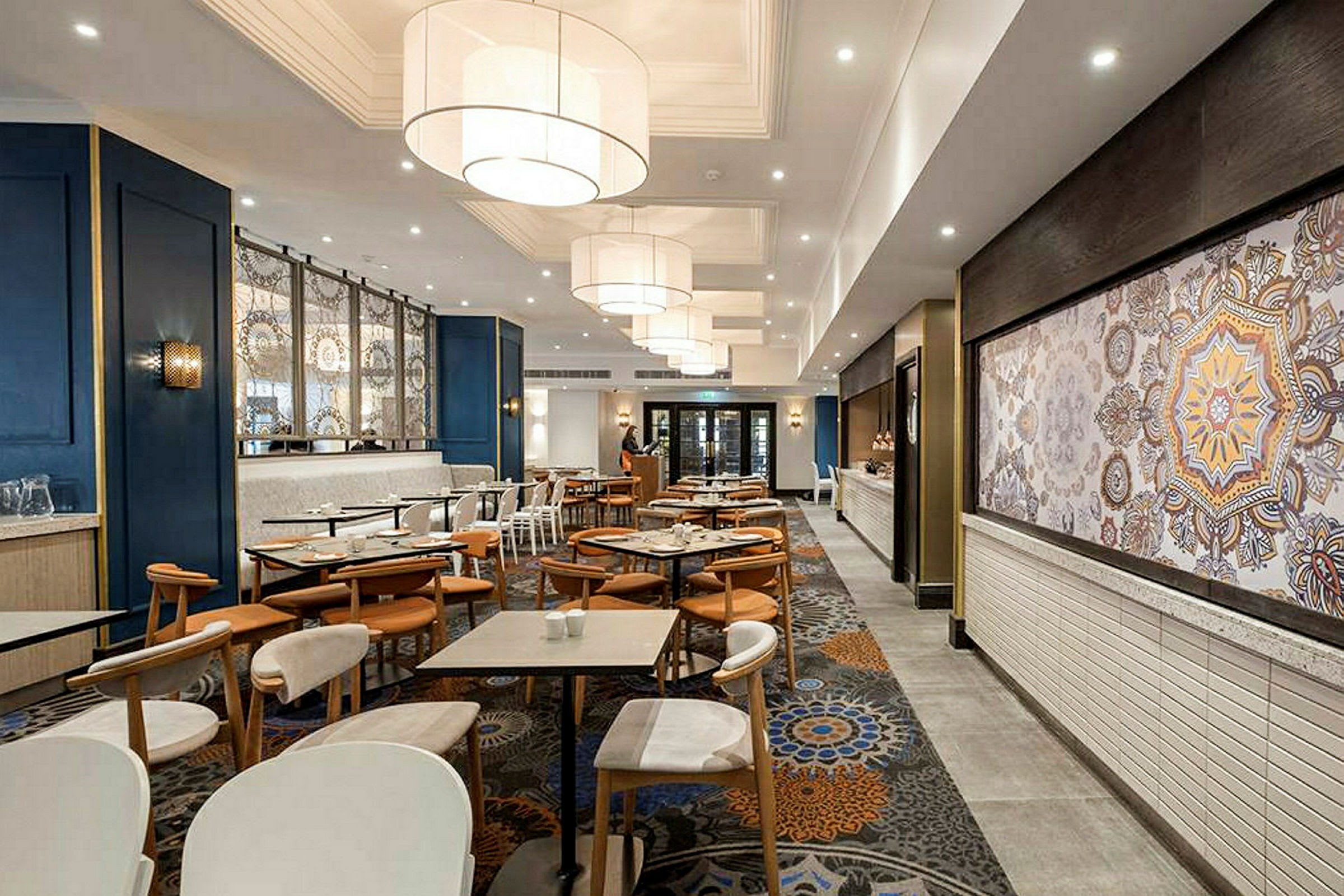 En restaurant med bord og stoler, moderne innredning og store lamper i taket. (AI-generert tekst)
