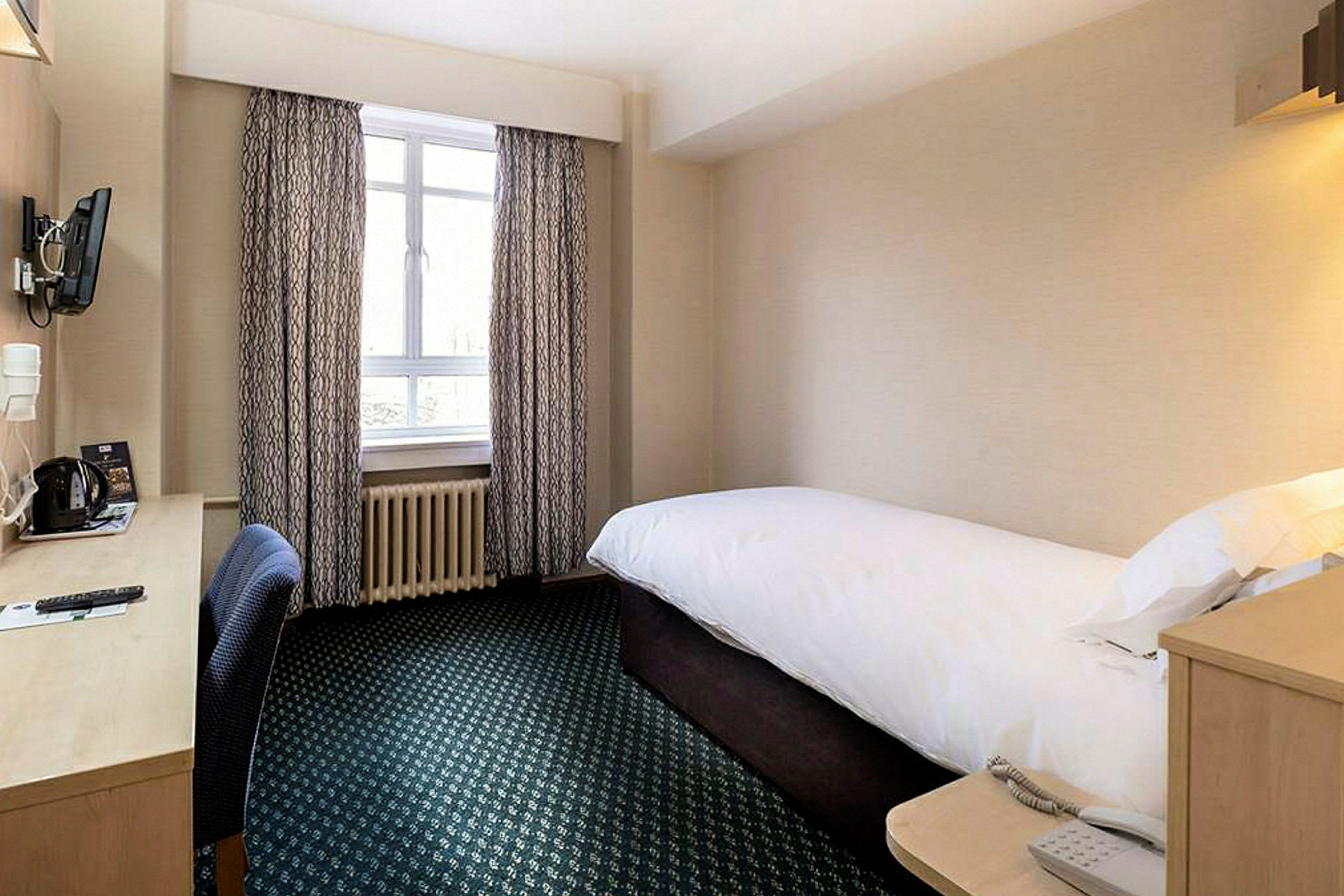 Et hotellrom med enkeltseng og skrivebord ved vinduet. (AI-generert tekst)