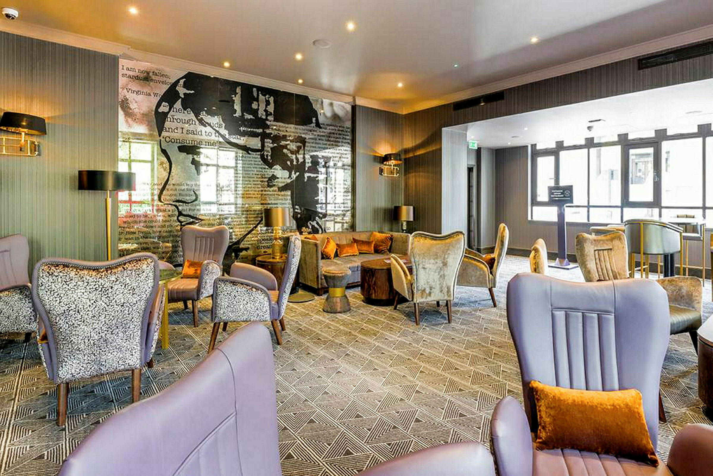 Et moderne hotellrom med komfortable sittemøbler, elegante dekorasjoner og en veggtapet med tekst og kunst. Store vinduer slipper inn naturlig lys. (AI-generert tekst)