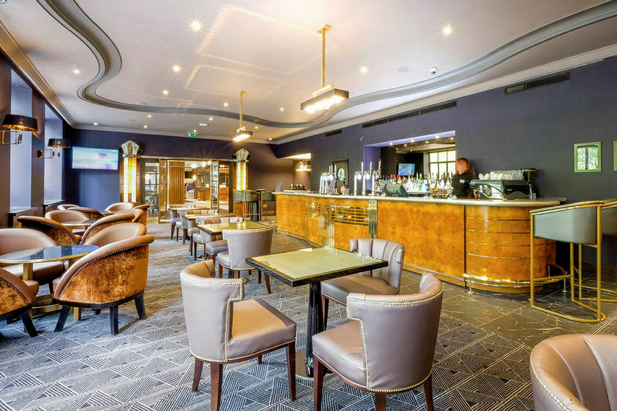 En hotellbar med bord og stoler samt en bardisk. (AI-generert tekst)