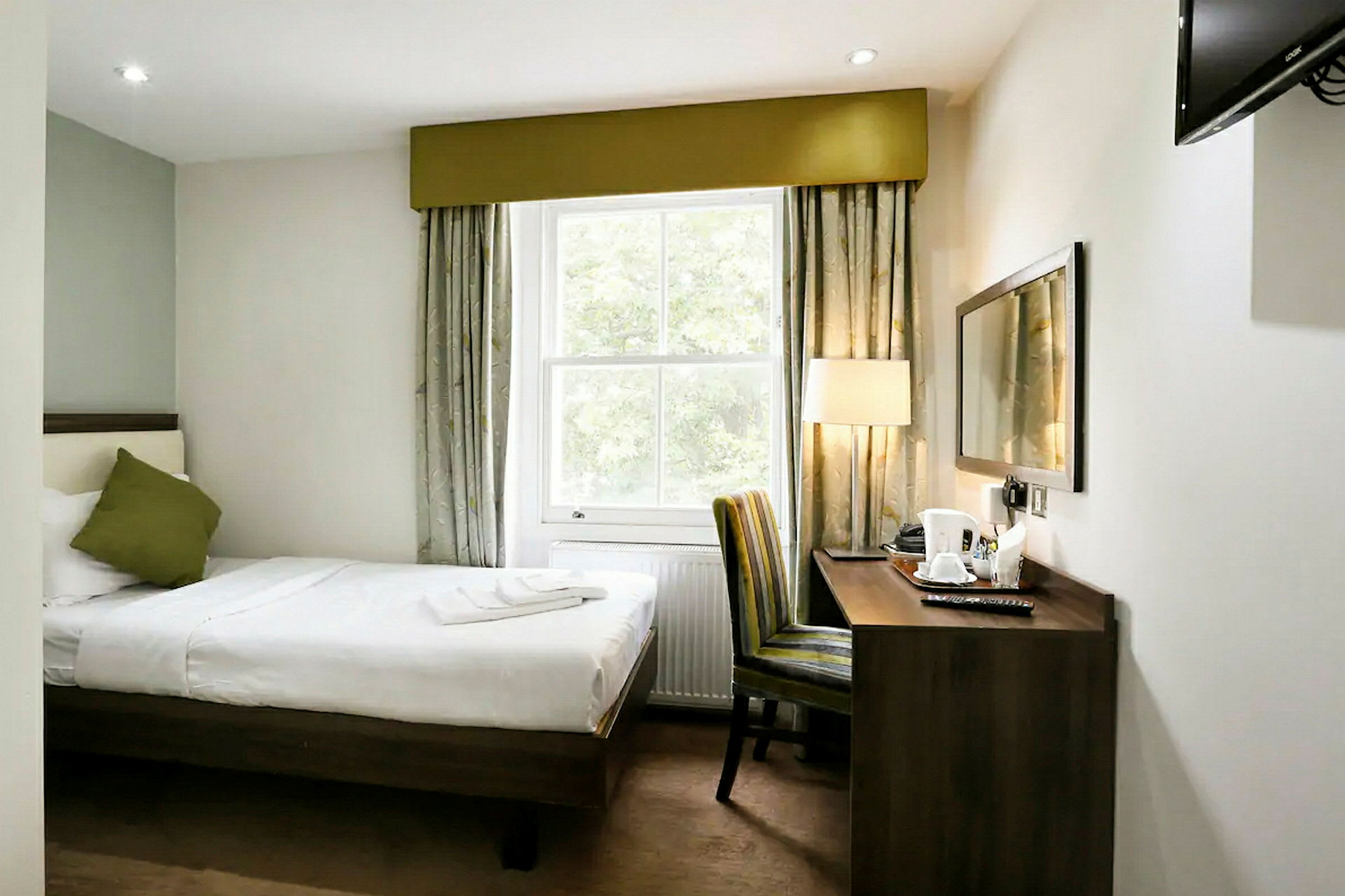 Hotellrom med enkeltseng, vindu, skrivebord og stol. (AI-generert tekst)