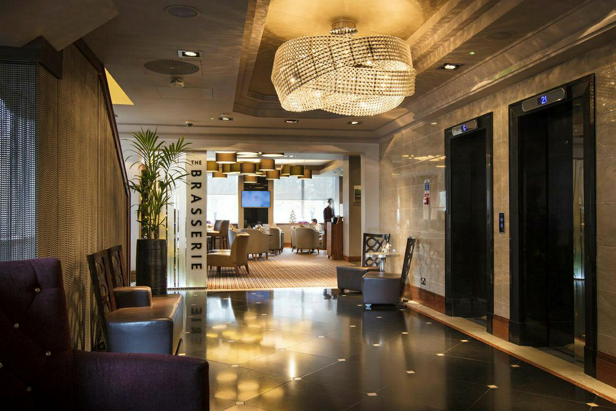 Hotellobby med heiser til høyre og inngang til restauranten 'The Brasserie' rett fram. (AI-generert tekst)