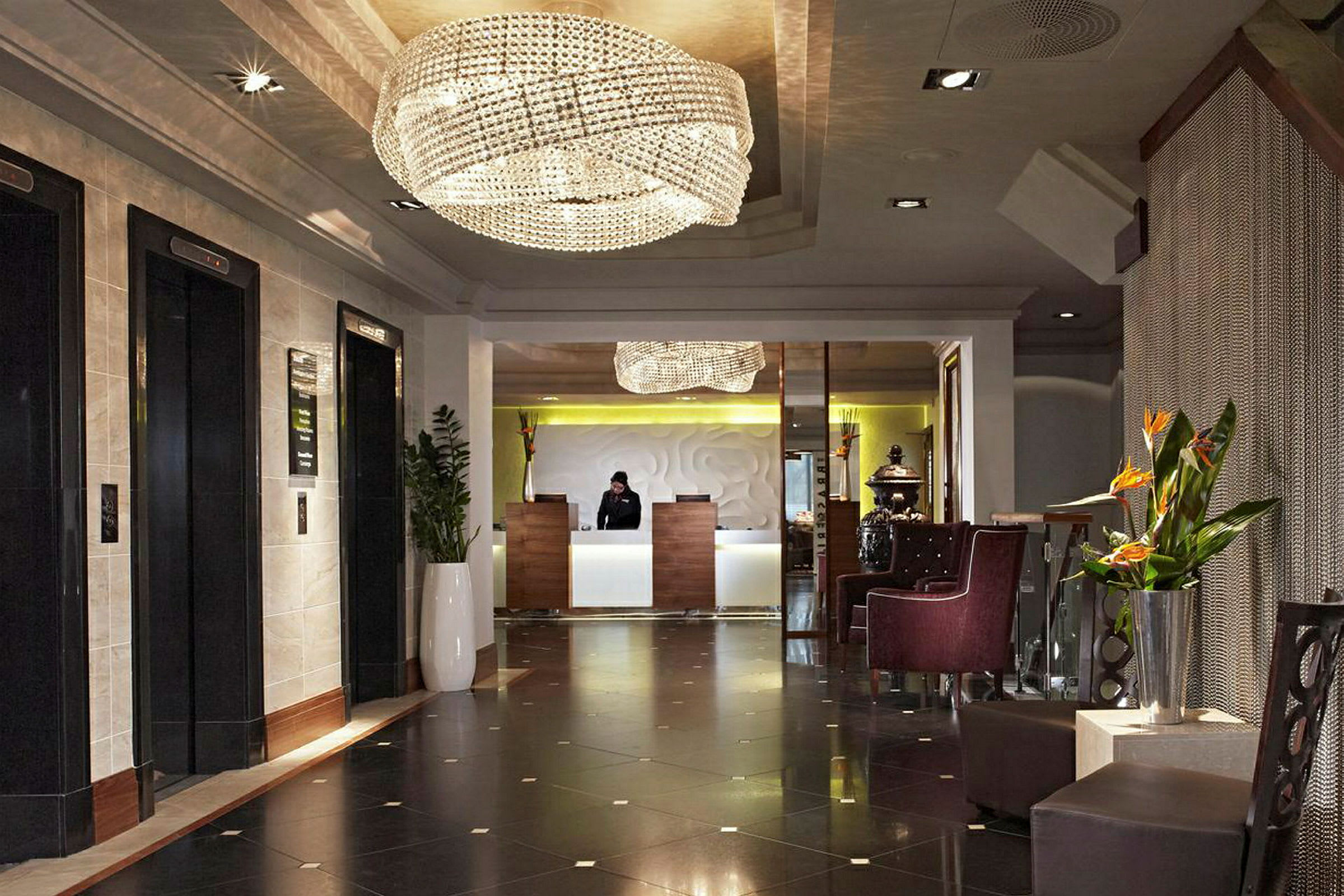 Hotellfoajé med resepsjon og venteområde, dekorert med lysekrone og planter. (AI-generert tekst)