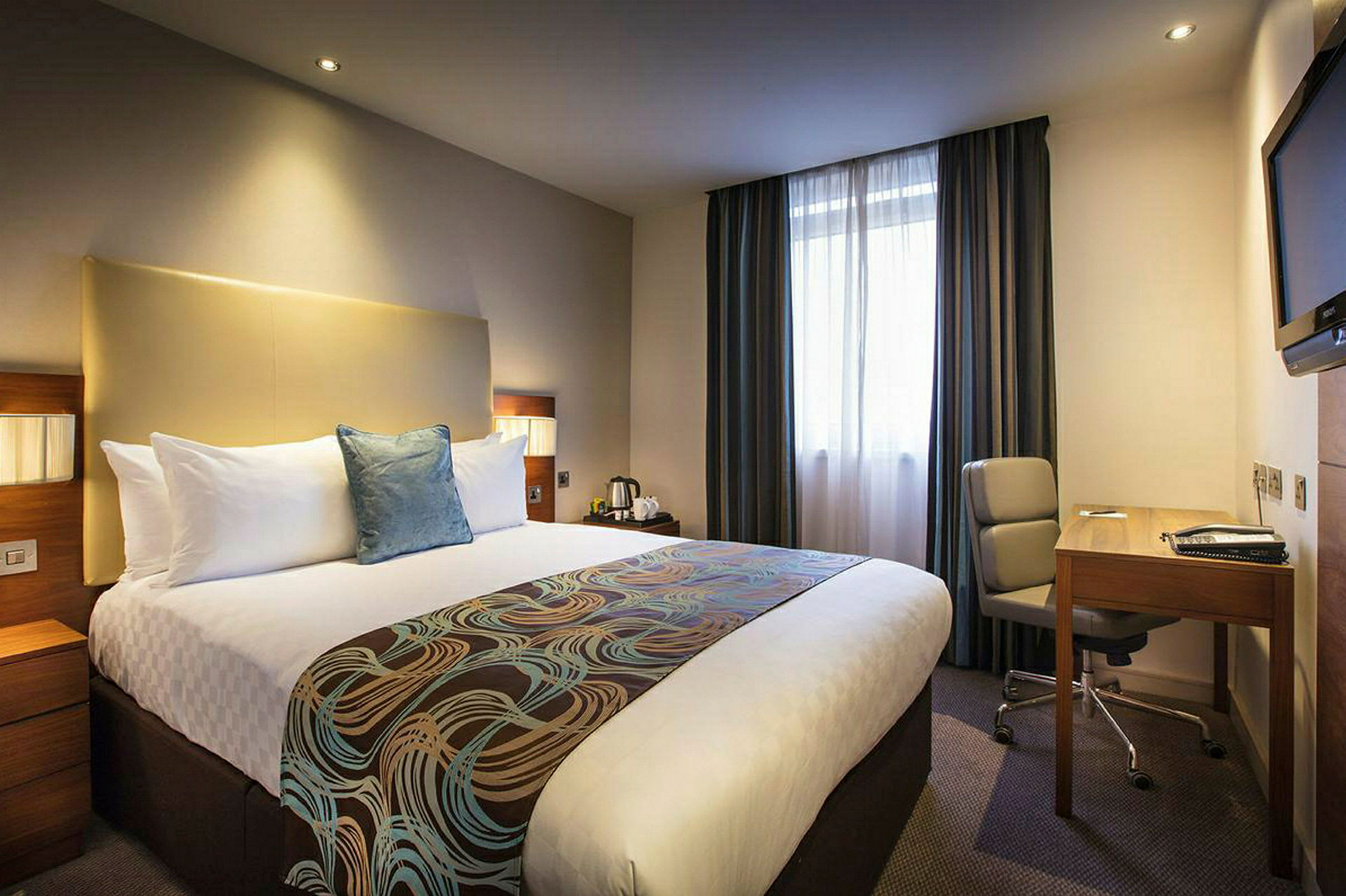 Hotellrom med en stor seng, skrivebord og stol. (AI-generert tekst)