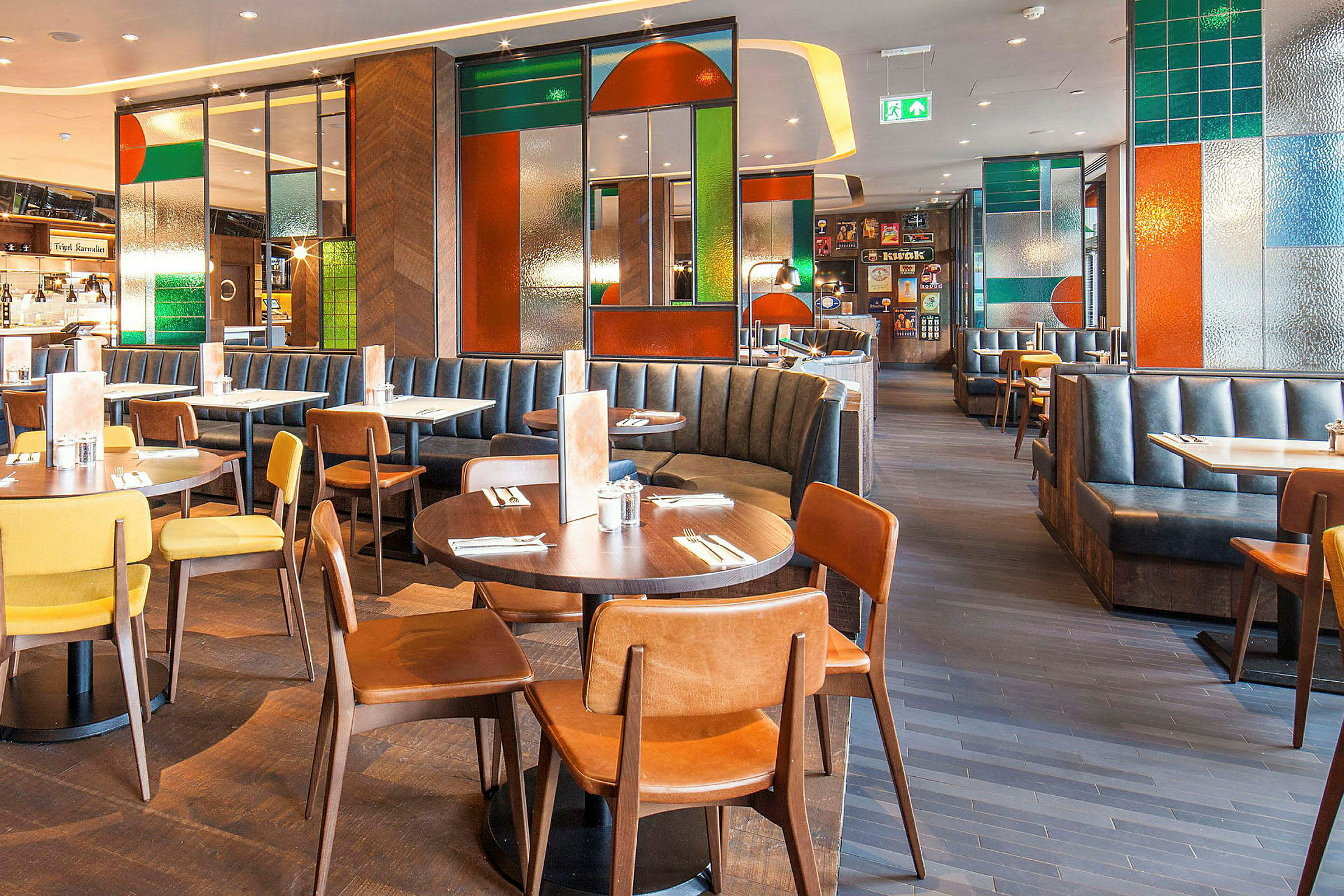 En restaurant med bord, stoler og båser, innredet med fargede glassdetaljer. (AI-generert tekst)