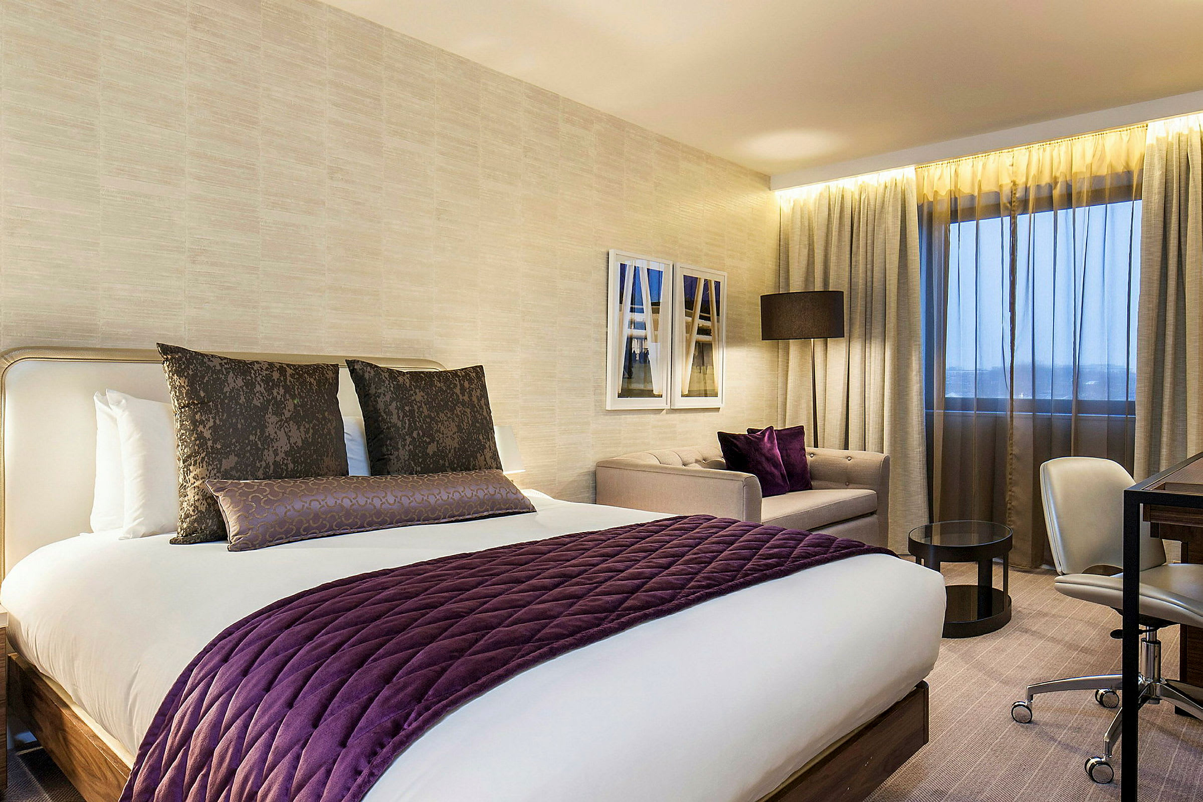 Et hotellrom med moderne innredning, inkludert en stor seng med lilla detaljer, en sittegruppe og skrivebord. (AI-generert tekst)