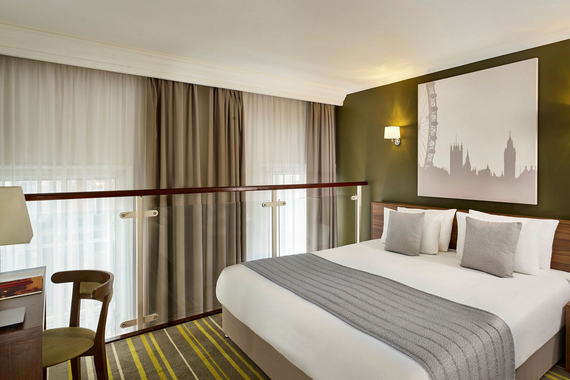 Et hotellrom med en dobbeltseng, grå puter og et bilde av Londons skyline på veggen. (AI-generert tekst)