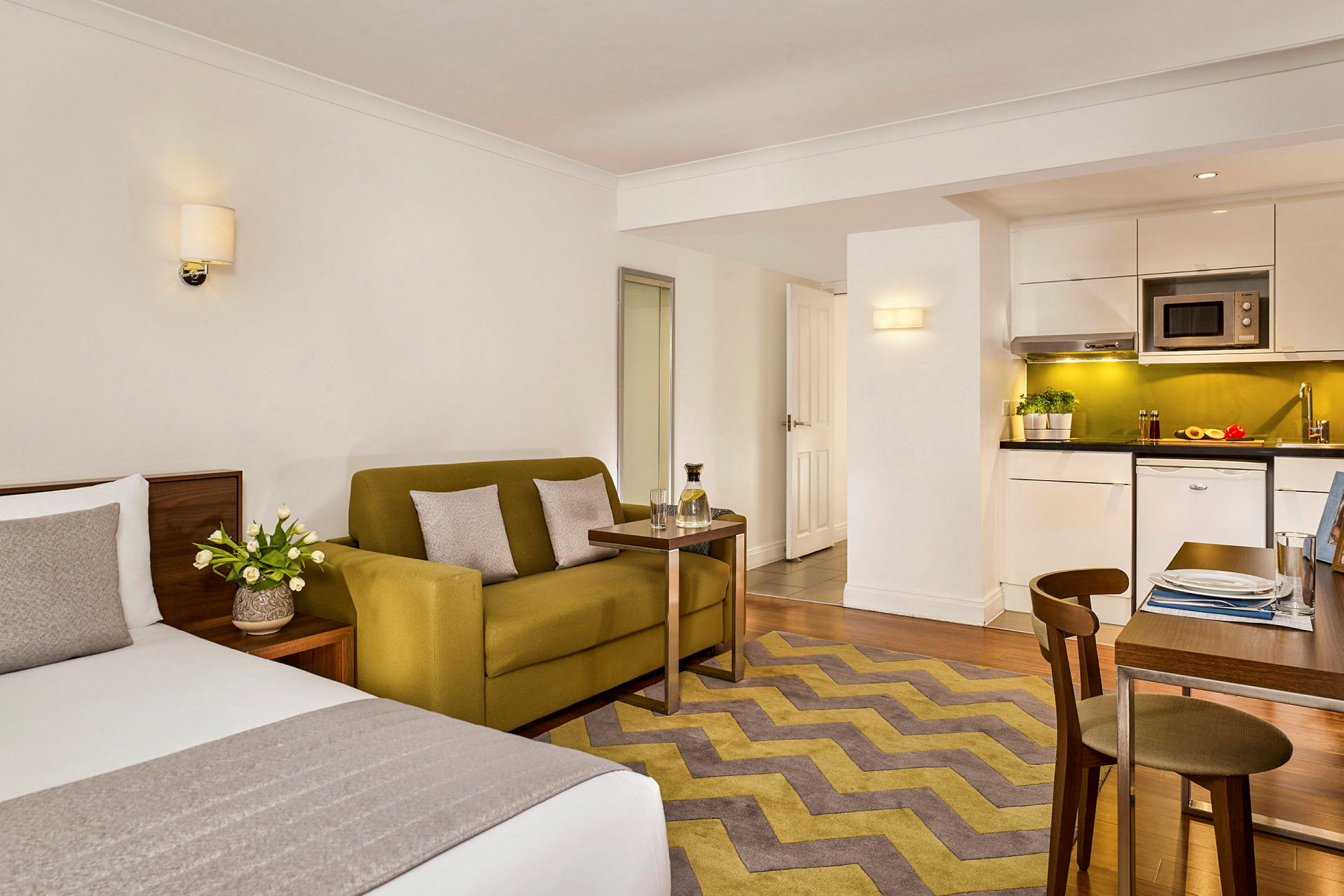 Et moderne hotellrom med seng, sofa, bord og et kjøkken med spiseplass. (AI-generert tekst)