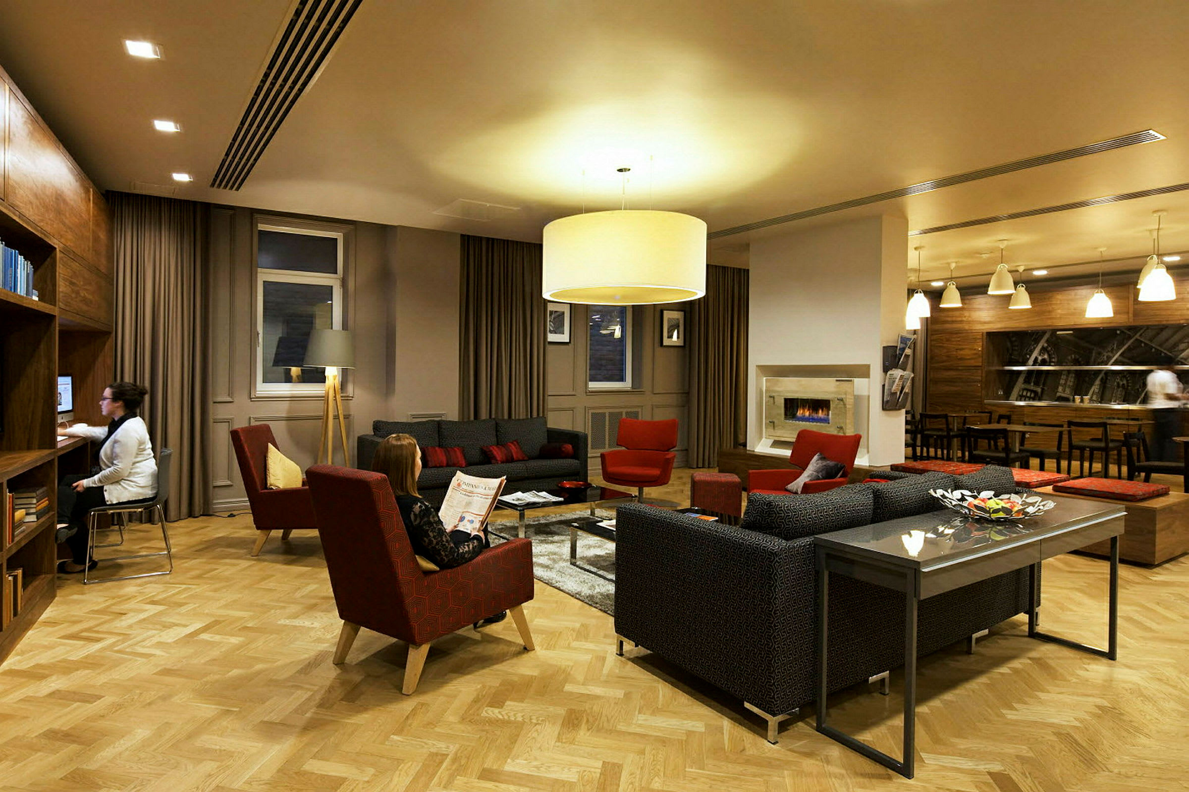 Et elegant oppholdsrom med sofaer, lenestoler og et sofabord omgitt av varm belysning og moderne innredning. (AI-generert tekst)