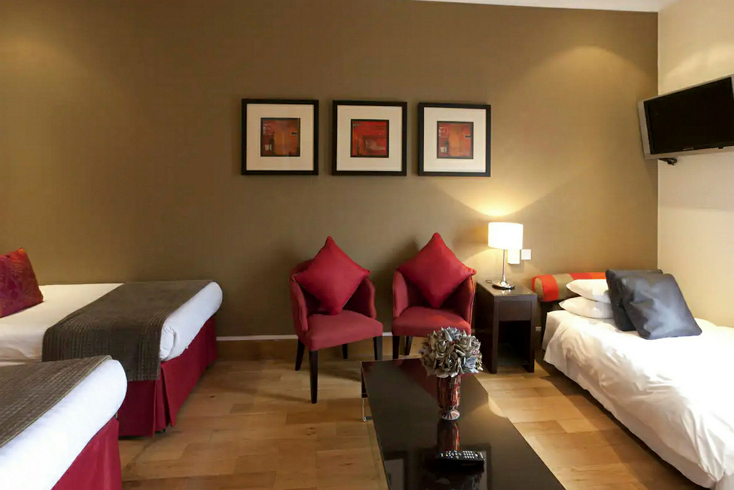 Hotellrom med to enkeltsenger, to røde stoler og et bord med blomster. (AI-generert tekst)