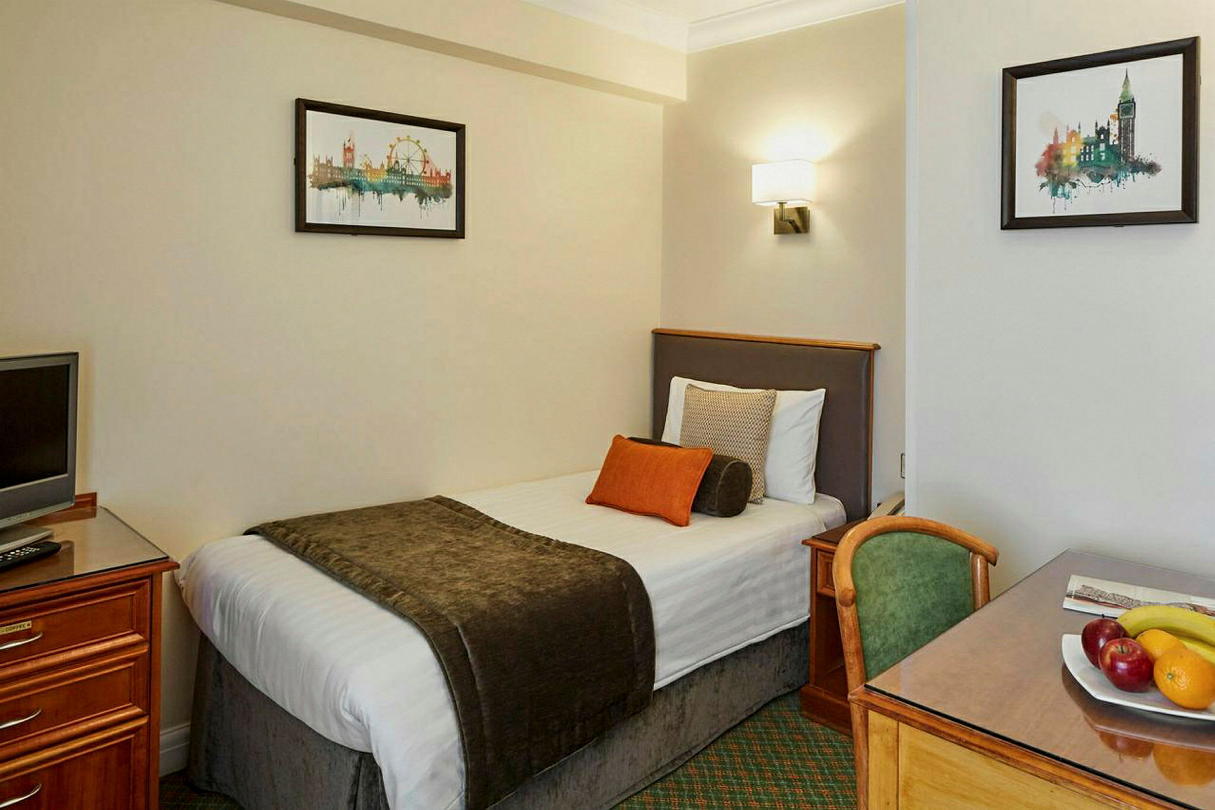 Hotellrom med enkeltseng, skrivebord, stol og dekorativ kunst på veggen. (AI-generert tekst)