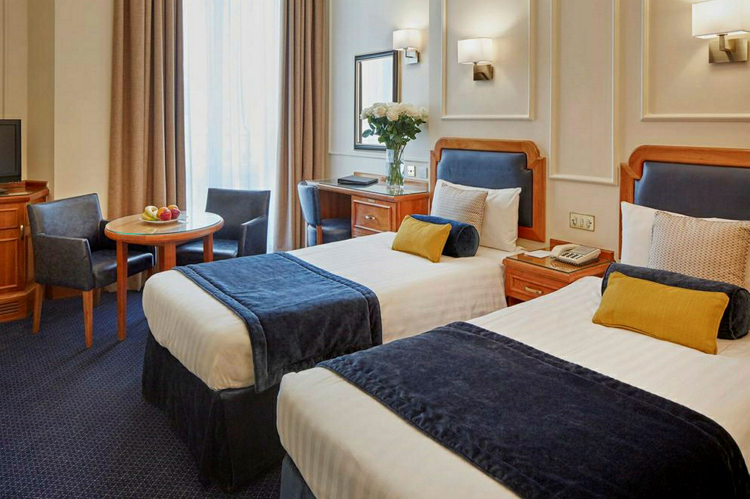 Hotellrom med to enkeltsenger, bord og stoler. (AI-generert tekst)